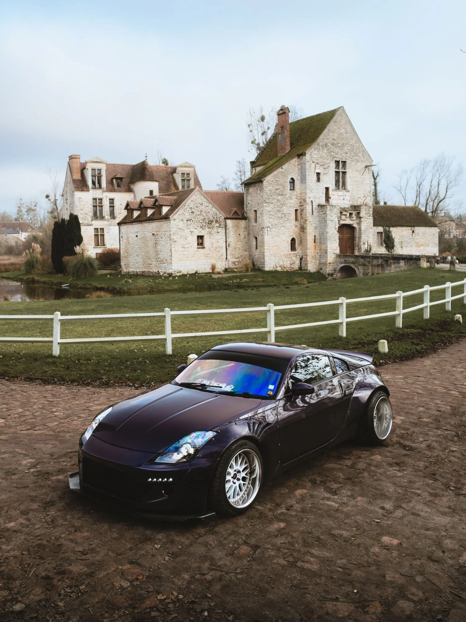 Une voiture noire de sport devant un vieux château en pierre sur fond de ciel clair.