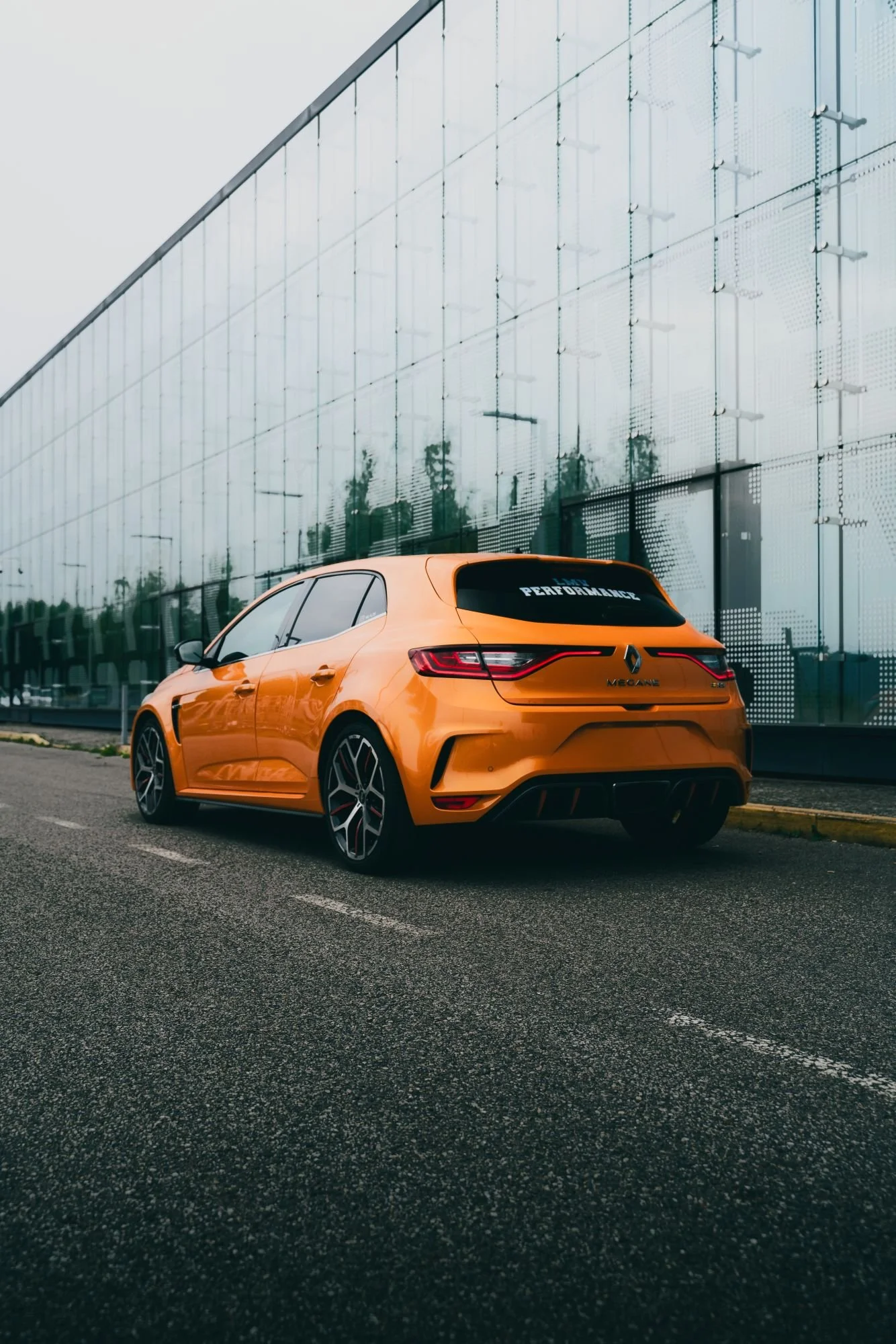 Voiture orange de sport stationnée sur une route près d'un bâtiment en verre moderne.
