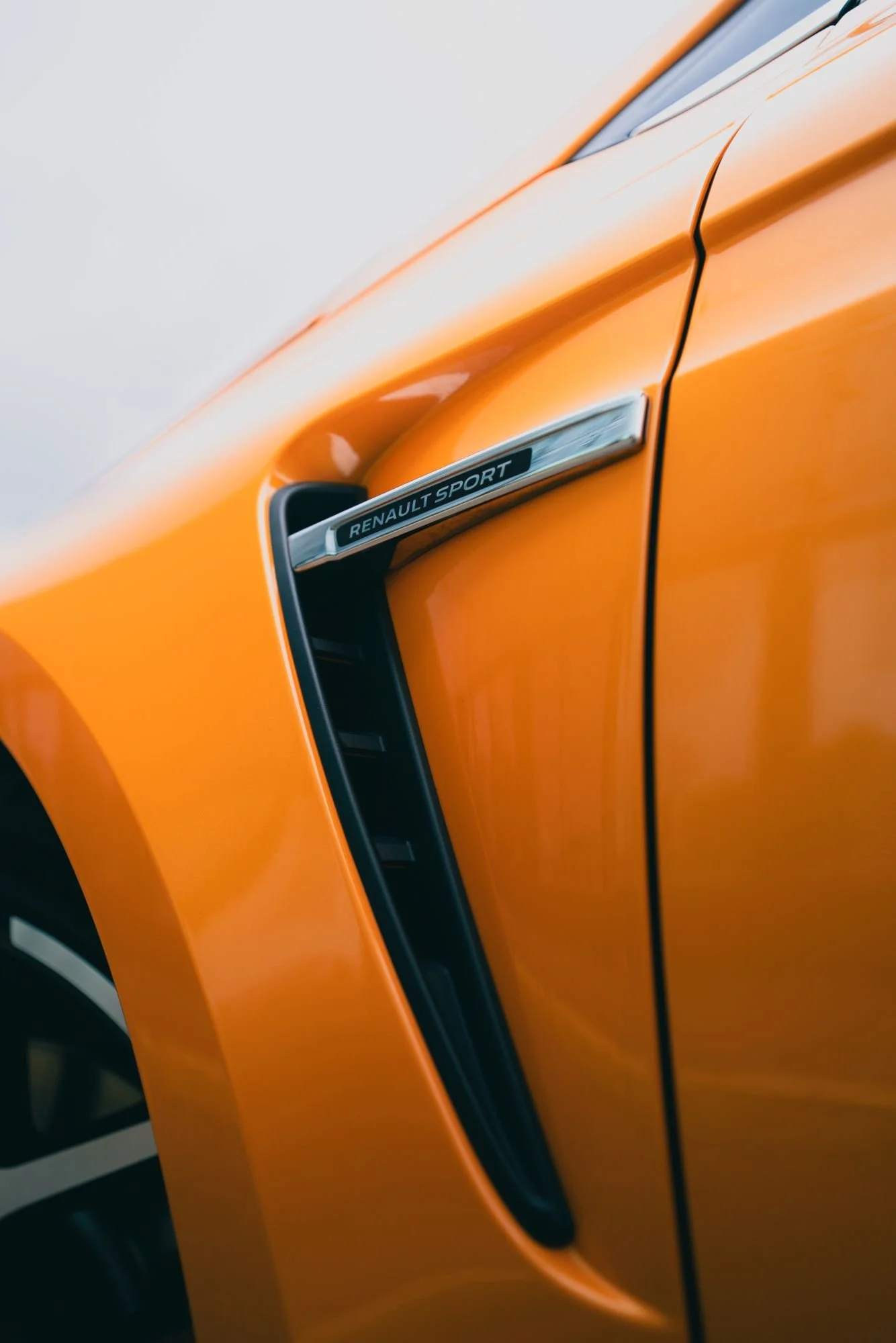 Voiture orange Renault Sport avec un détail de la carrosserie et le badge Renault Sport visible.