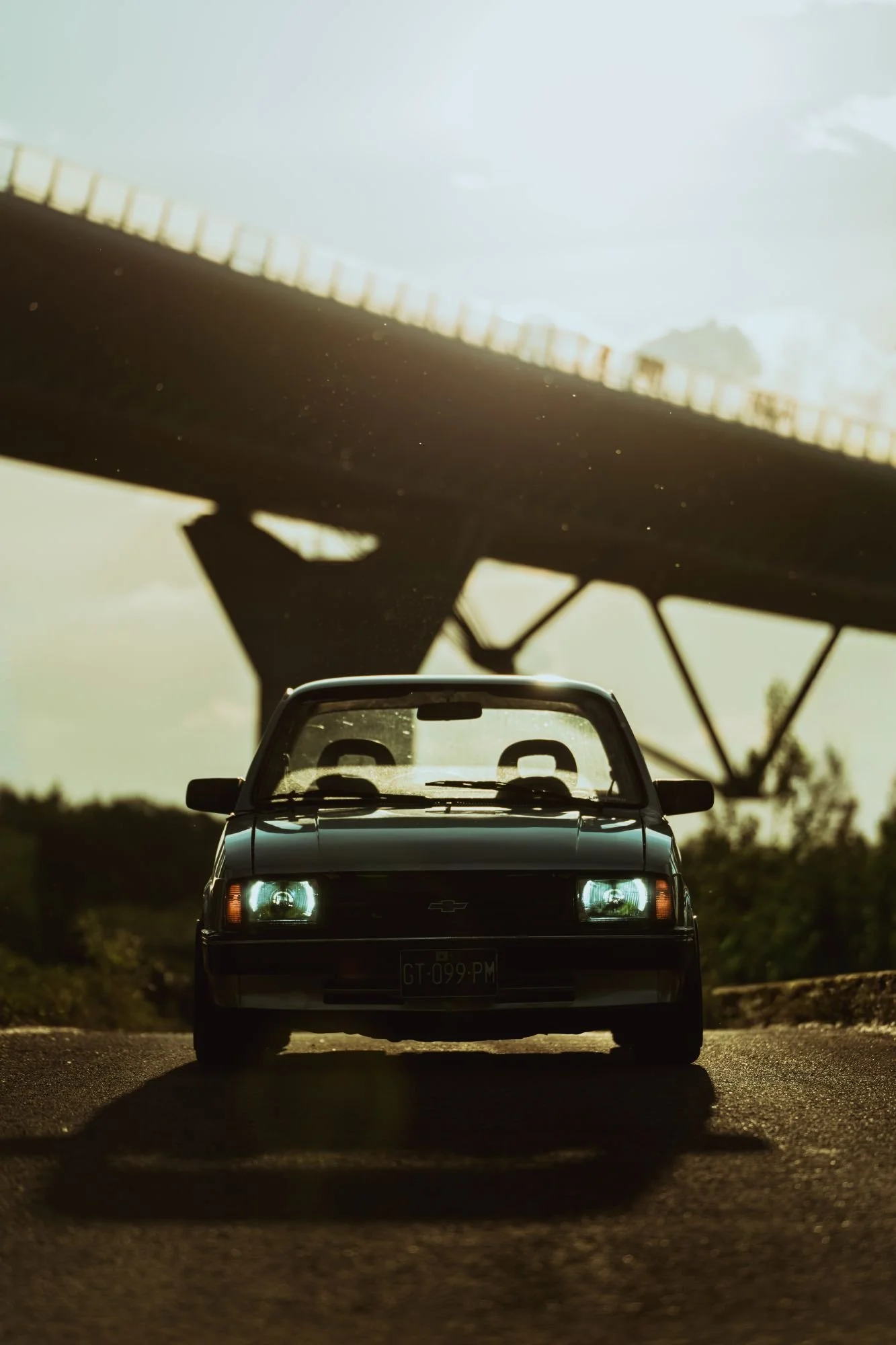 Une photo d'une voiture noire garée sur une route, avec un pont en arrière-plan sous un ciel ensoleillé.