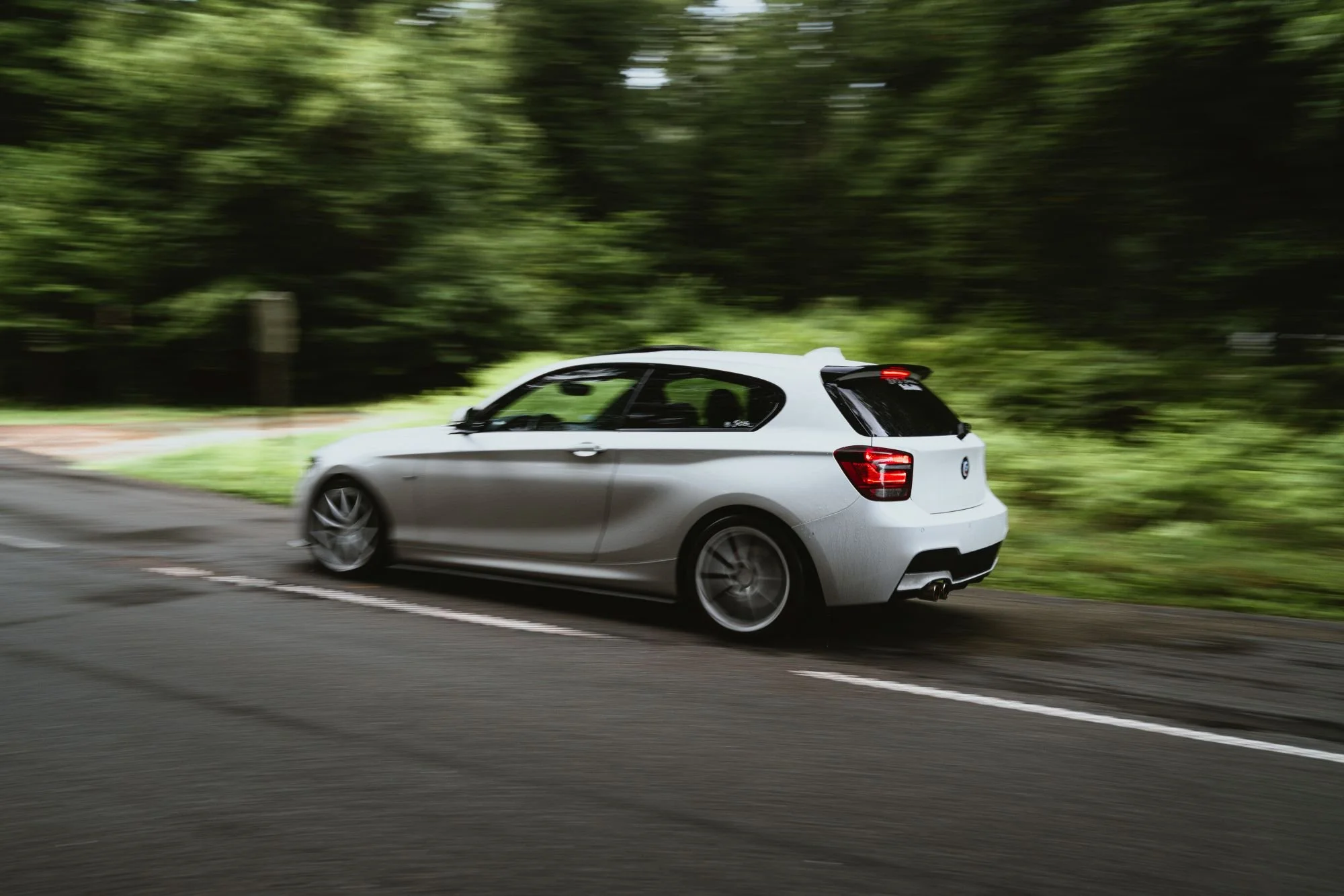 Voiture blanche roulant sur une route bordée d'arbres verts, avec un arrière-plan flou indiquant la vitesse.