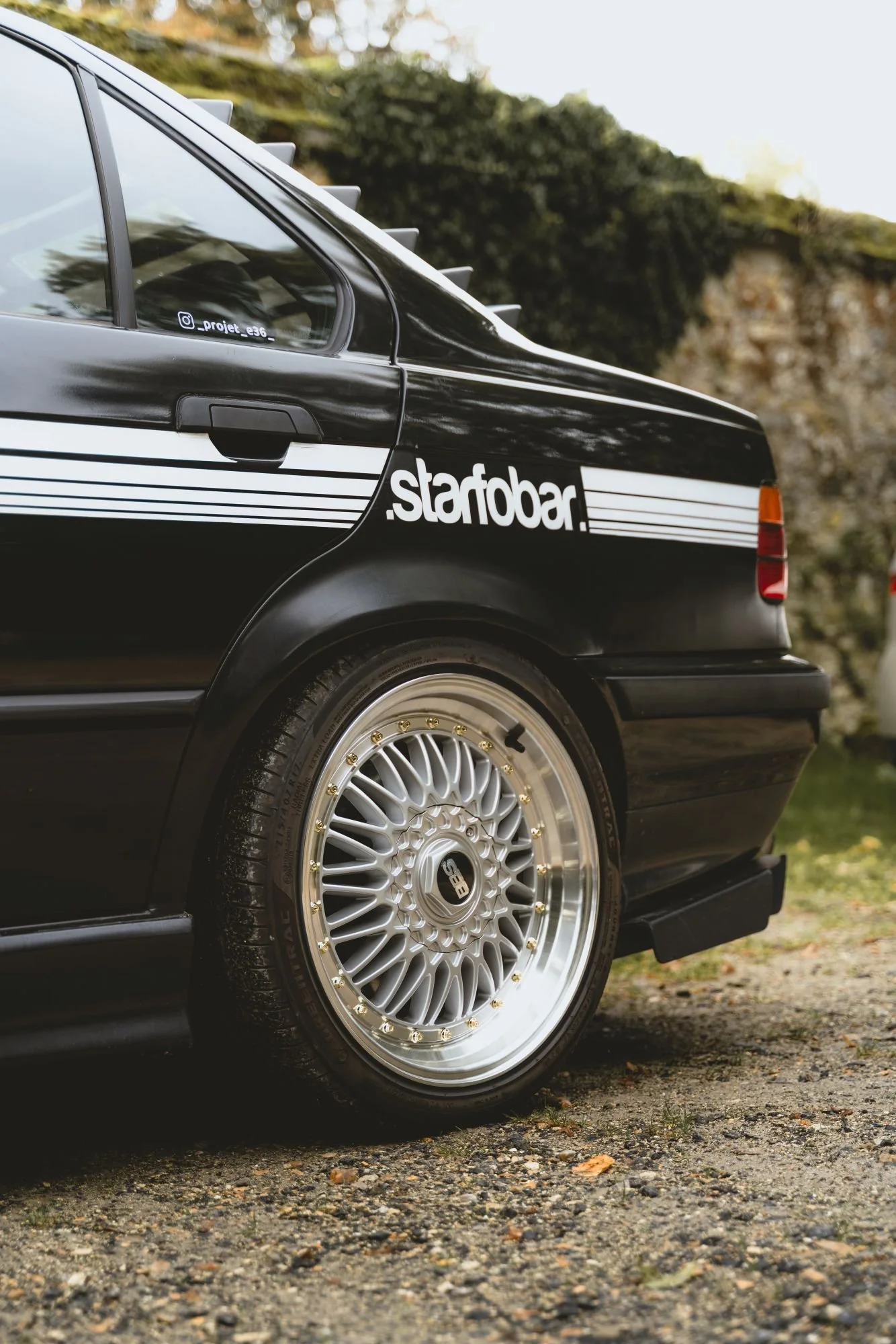 Voiture noire avec un pare-chocs arrière et une roue en alliage à rayons multiples.