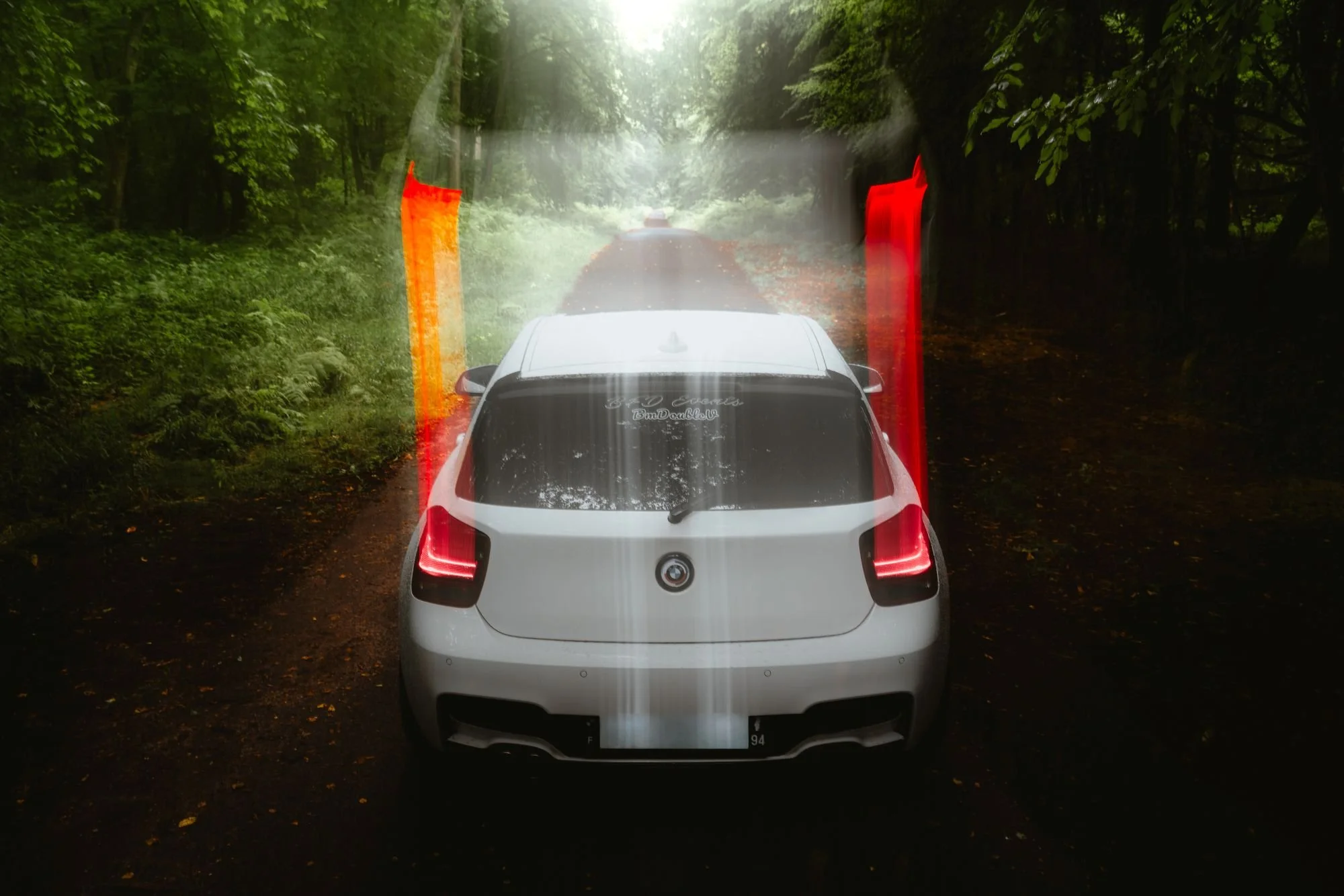 Une voiture blanche vue de derrière, dans une forêt, avec des lignes rouges et jaunes indiquant un point d'arrêt ou une zone de contrôle.