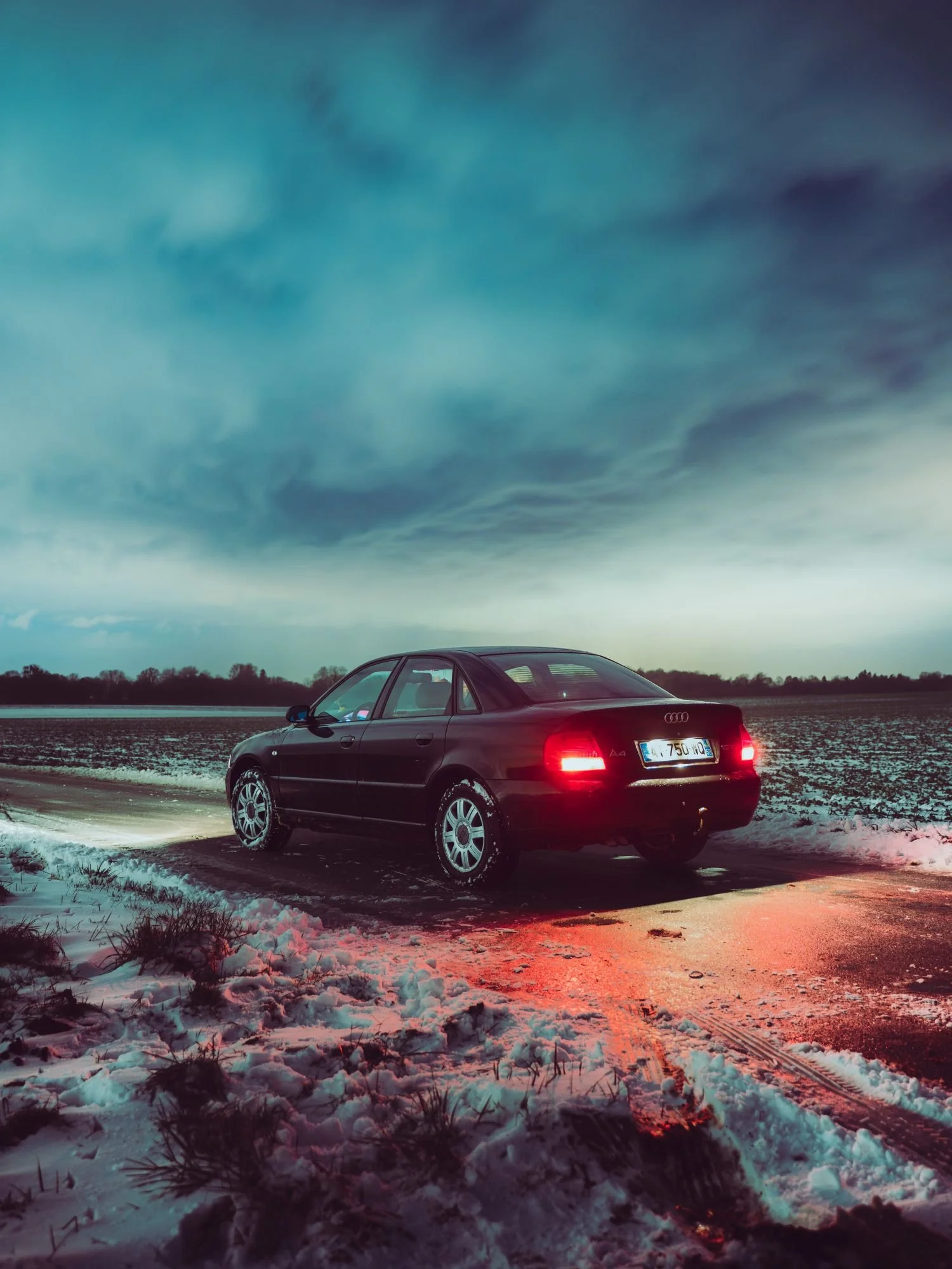 Voiture noire Audi A4 garée sur une route enneigée lors d'un coucher de soleil ou d'une journée nuageuse.