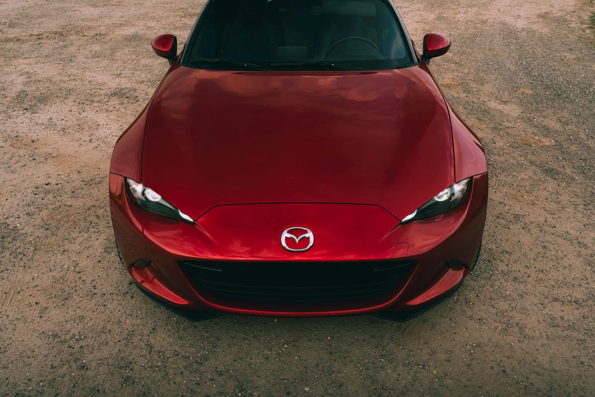 Voiture rouge de marque Mazda vue de face sur un sol en terre.