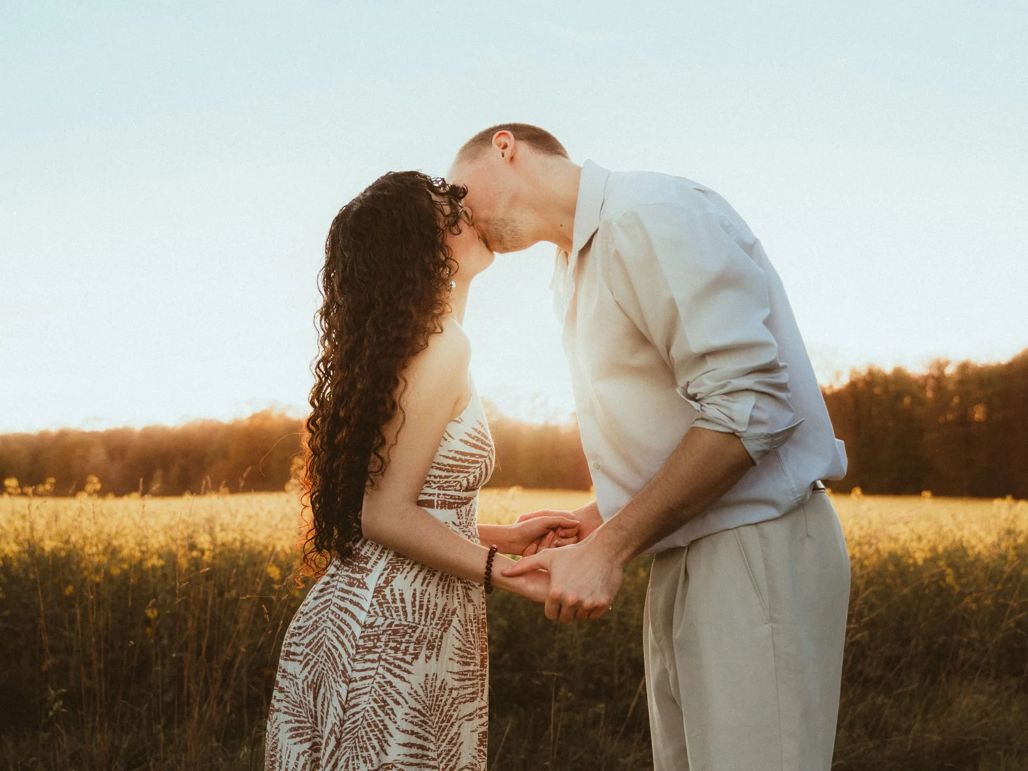Un couple s'embrasse dans un champ au coucher du soleil.