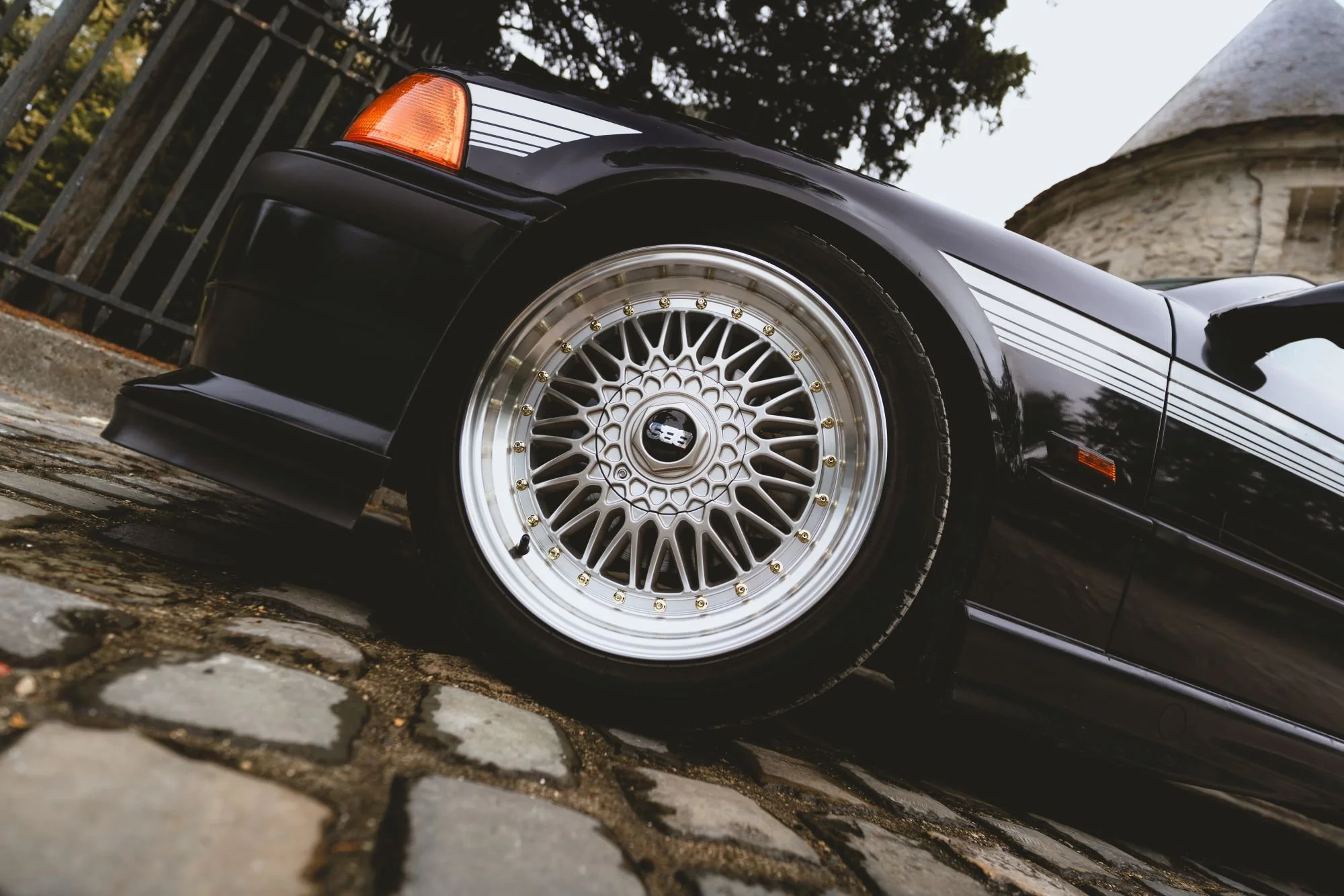 Voiture noire avec des jantes en alliage et des bandes décoratives, vue de côté sur une surface pavée.