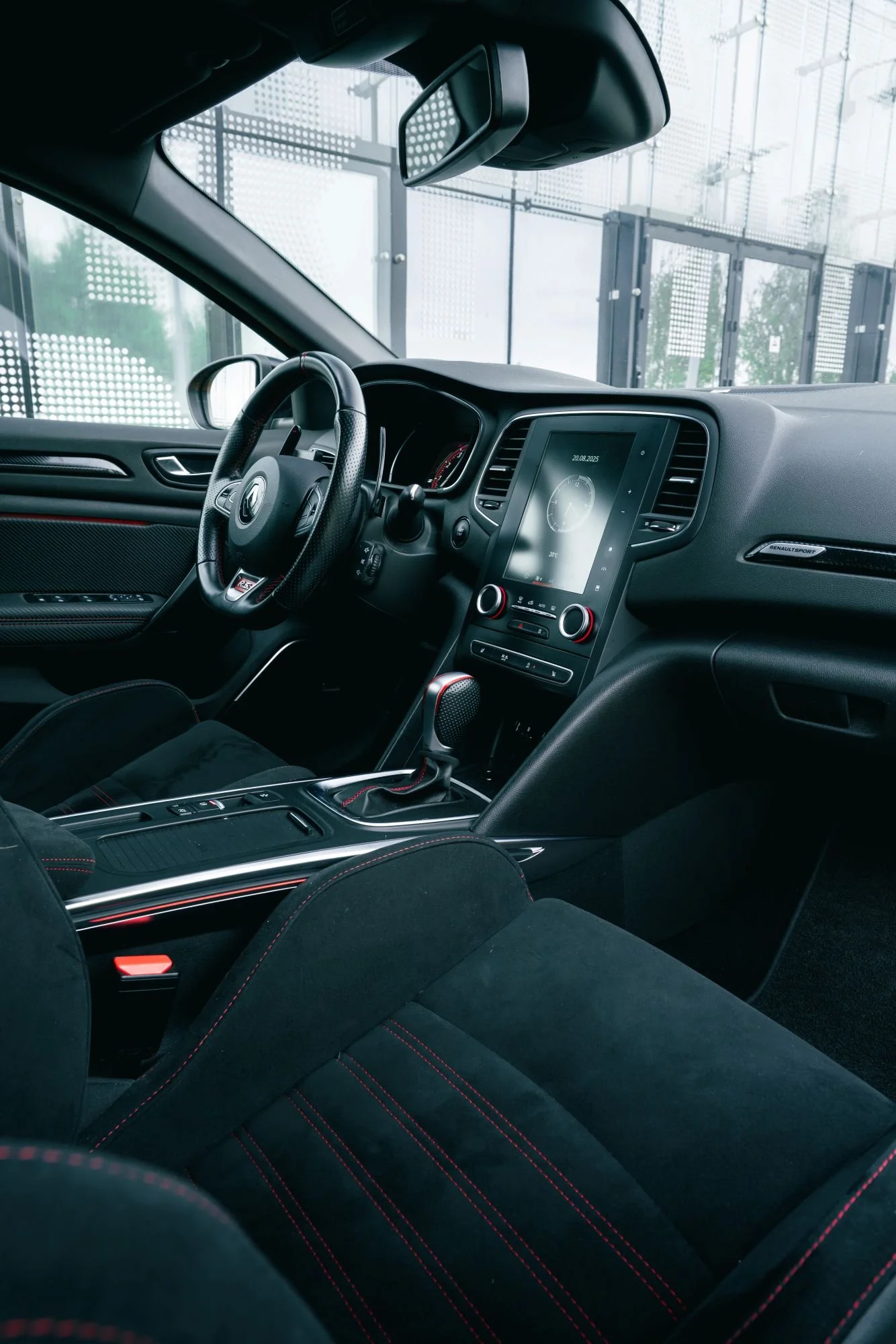 Intérieur d'une voiture de sport noire avec un tableau de bord numérique et un siège en tissu noir avec des coutures rouges.