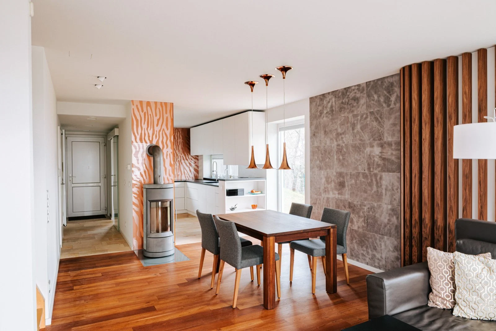 Moderne Wohnküche mit Essbereich, offenem Wohnkonzept, warmem Holzboden, Designwand, Holzlamellen und stilvoller Innenarchitektur für hochwertiges Wohnen