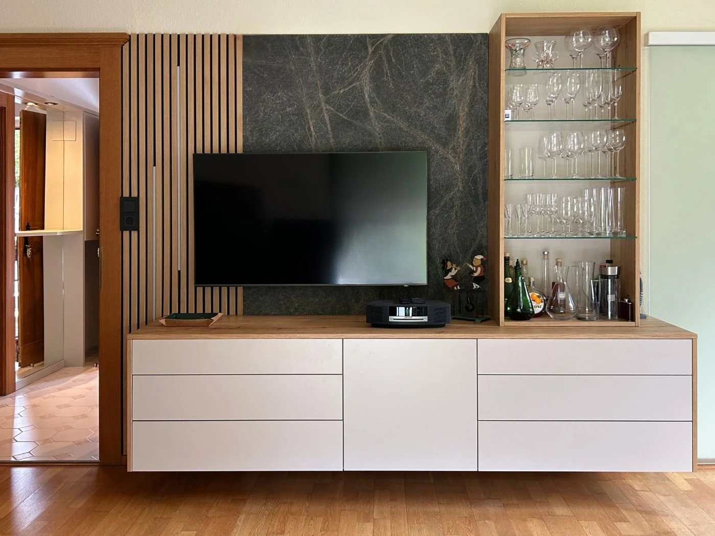 Wohnwand nach Maß mit TV, weißen Unterschränken und beleuchteter Glasvitrine
