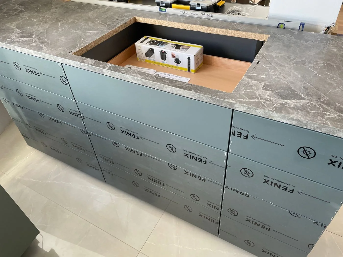 Kücheninsel während der Montage: Arbeitsplatte in Marmoroptik mit Ausschnitt für ein flächenbündiges Induktionskochfeld, Fronten mit Schutzfolie - Küchenmontage und Küchenplanung in Wien und Umgebung