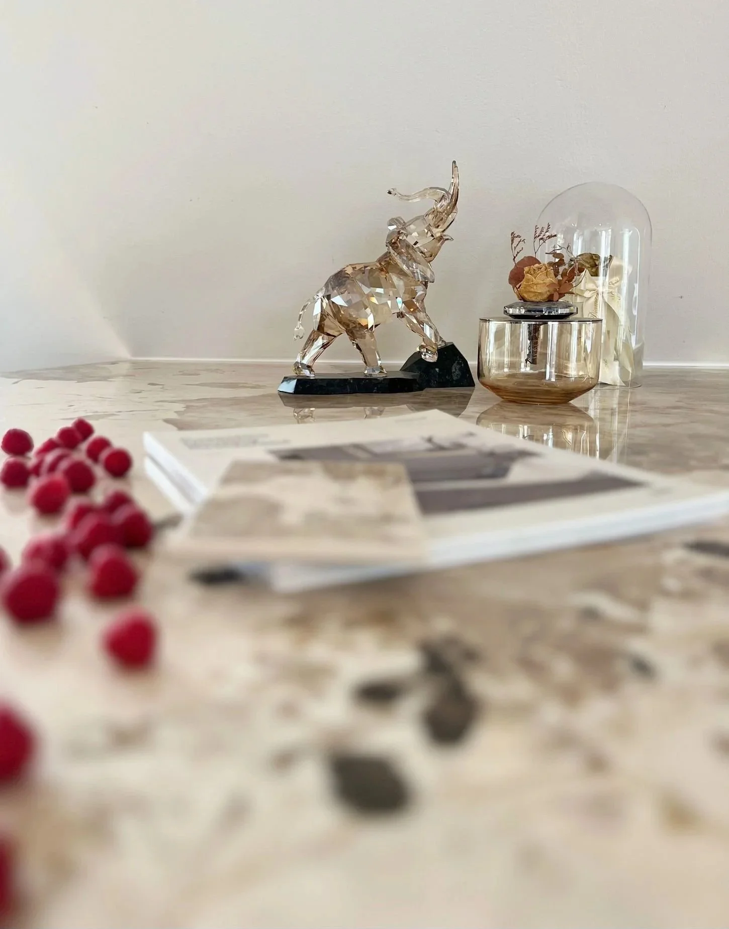 Atmosphärische Detailaufnahme einer hellen Dekton-Arbeitsplatte Khalo von Cosentino in Marmoroptik mit Hembeerne und einer Elefant-Glasfigur als Dekoration - Kücheninspiration, Materialauswahl, Küchenplanung und Küchenmontage in Wien und Umgebung
