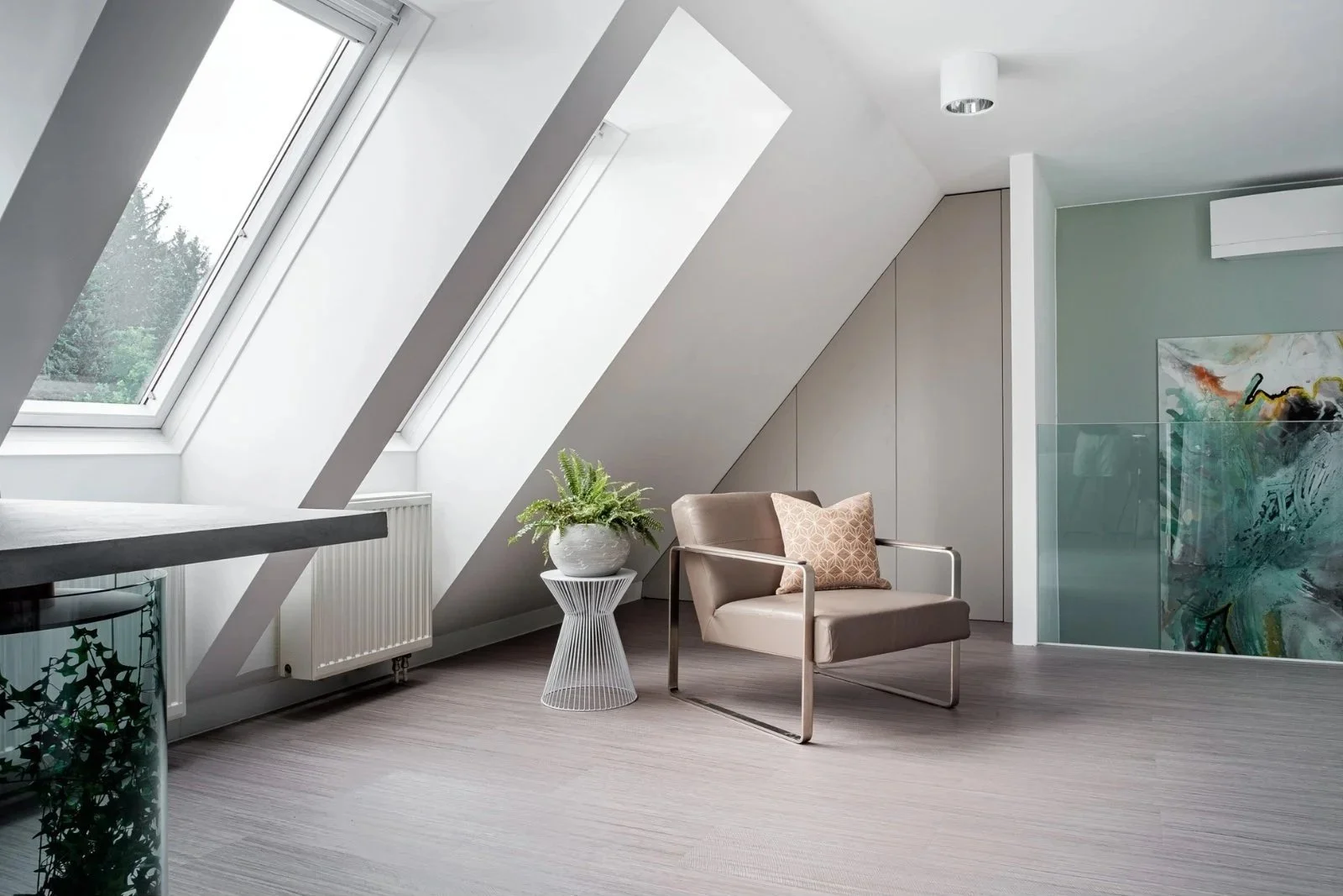 Heller Raum unter Dachschrägen mit großem Dachfenster, Sessel und kleinem Beistelltisch.