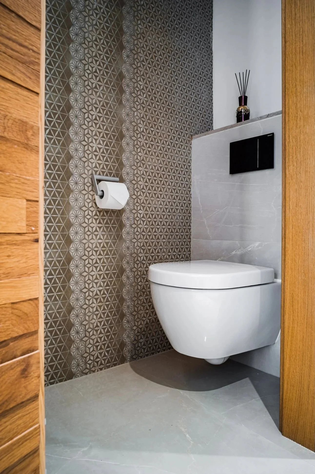 Modernes Gäste-WC mit wandhängendem WC, dekorativer Musterfliesenwand und warmen Holzdetails – stilvolle Badgestaltung mit klarer Linienführung, hochwertiger Materialkombination und elegantem, kompaktem Raumkonzept