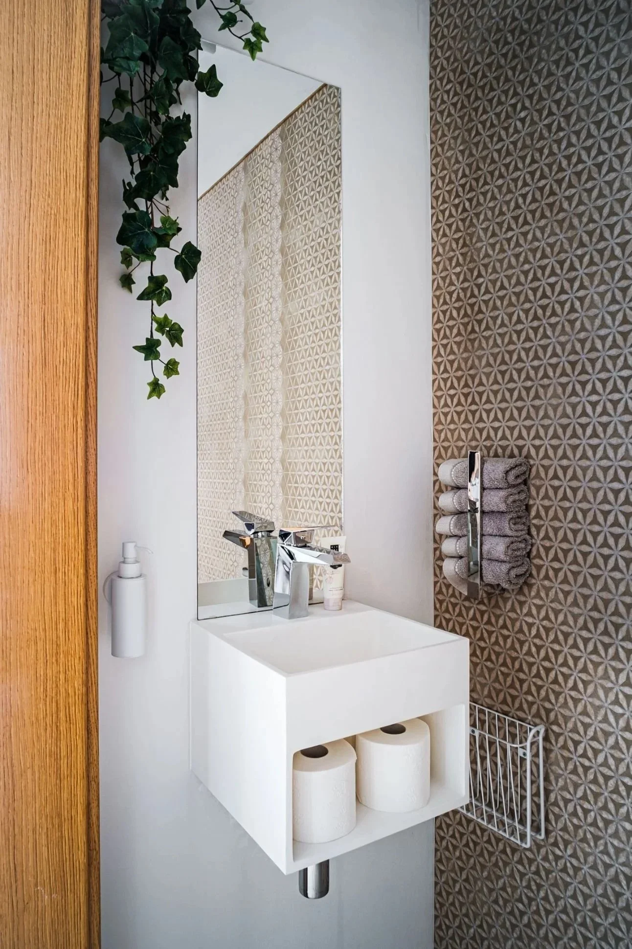 Modernes Gäste-WC mit kompaktem Waschbecken, Spiegel, dekorativer Musterfliesenwand und warmen Holzdetails – hochwertiges Badinterieur mit platzsparender Gestaltung, klarer Formensprache und stilvoller Atmosphäre