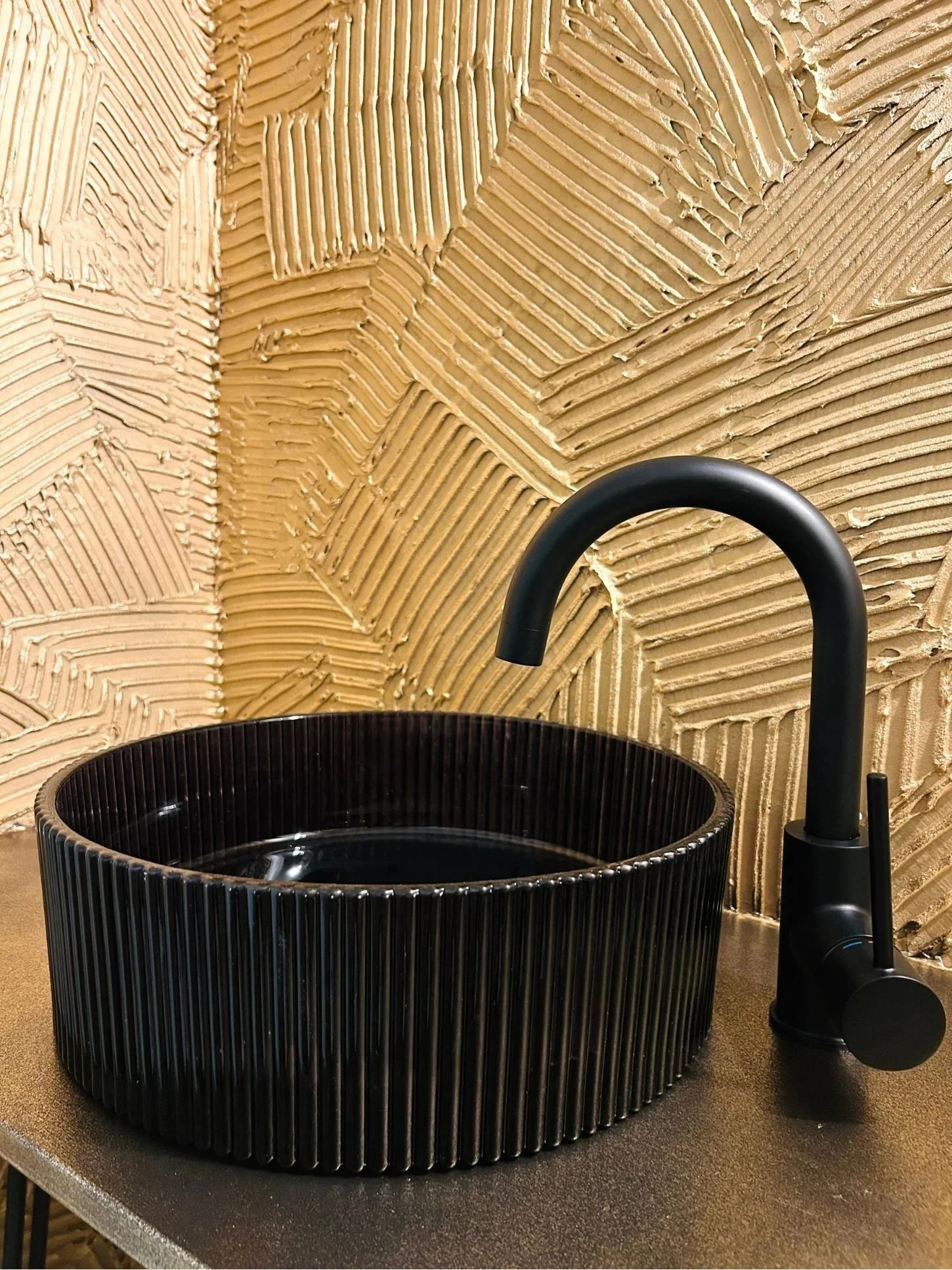Schwarzes Aufsatzwaschbecken vor einer goldfarbenen fugenlosen Wand