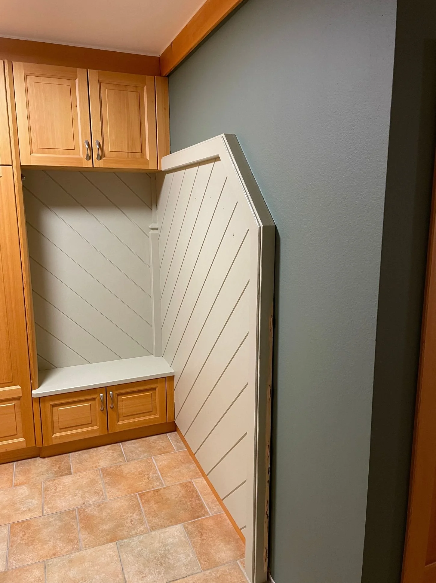 Nachher-Bild einer modernisierten Garderobe mit aufgearbeiteten Holzeinbauten, heller Sitzbank, grafischer Wandverkleidung und dunkler Akzentwand – aufgewerteter Eingangsbereich mit klarer Linienführung, mehr Ruhe und zeitgemäßer Innenarchitektur