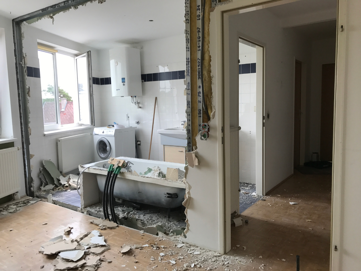 Vorher-Bild einer Badsanierung mit entkerntem Badezimmer, freigelegter Badewanne, Wanddurchbruch und Bauschutt im Bestandszustand – Ausgangssituation vor dem Badumbau und der Neugestaltung des Wohnraums