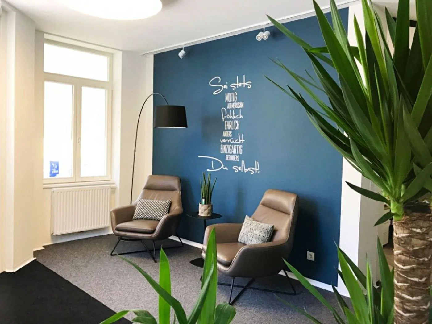Nachher-Bild eines modernisierten Kundeneingangsbereichs mit gemütlichem Wartebereich, blauer Akzentwand, Pflanzen und stilvoller Möblierung – einladend gestalteter Empfangsbereich mit mehr Offenheit, Persönlichkeit und professioneller Raumwirkung