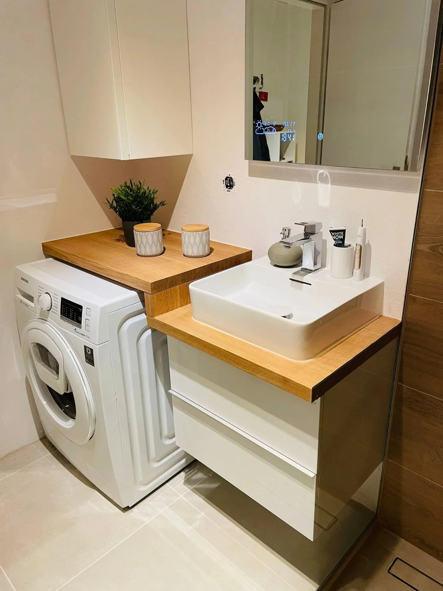 Nachher-Foto eines modernisierten Waschplatzes im Badezimmer mit integrierter Waschmaschine, neuer Holzplatte, Aufsatzwaschbecken und smartem Spiegel - Mini-Makeover von Paddy Artist Design GmbH