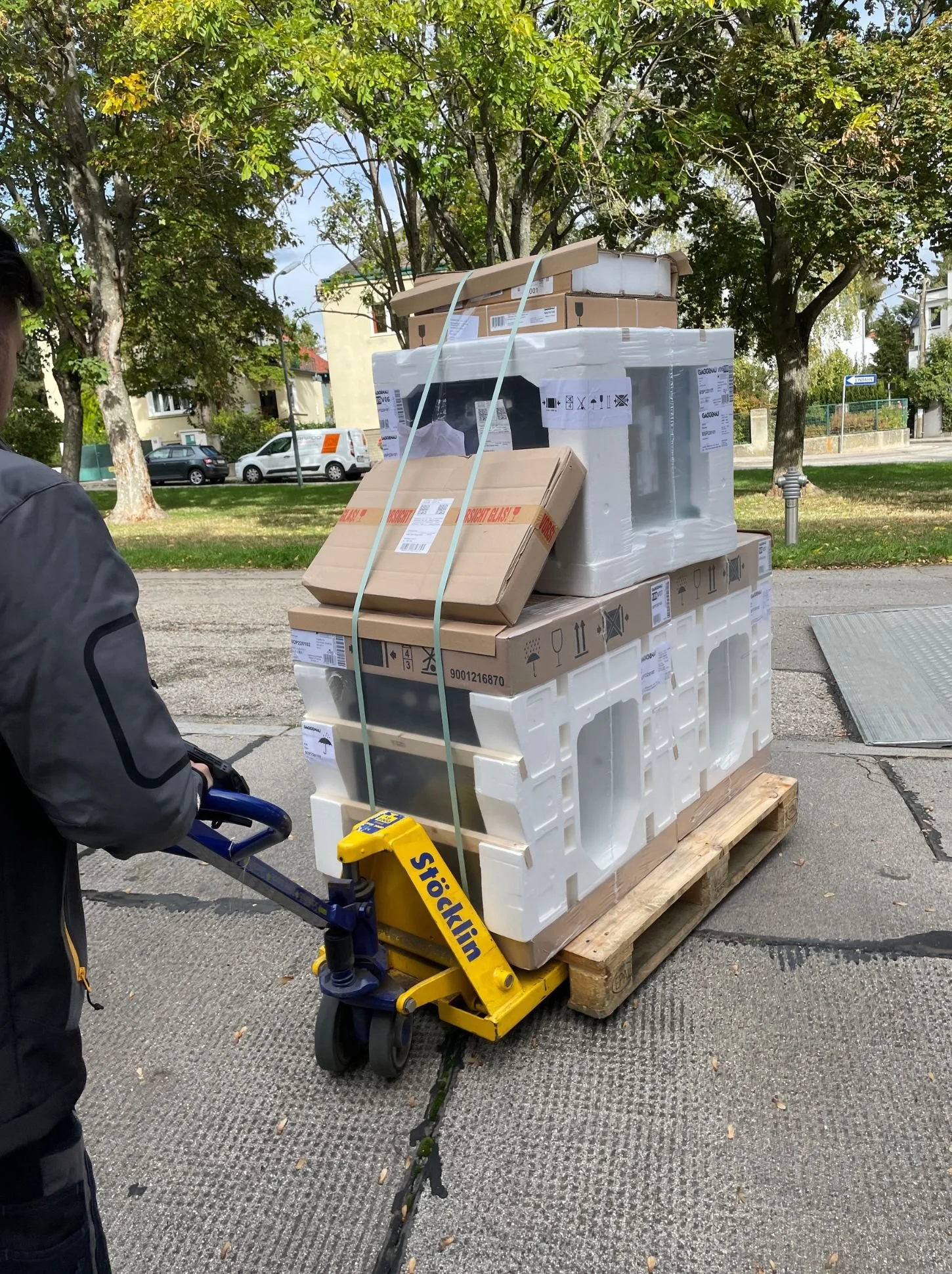 Anlieferung einer neuen Küche: Küchenmöbel und Geräte auf einer Palette, transportiert mit Hubwagen vor einem Wohnhaus - Küchenlieferung, Küchenmontage und Küchenplanung in Wien und Umgebung