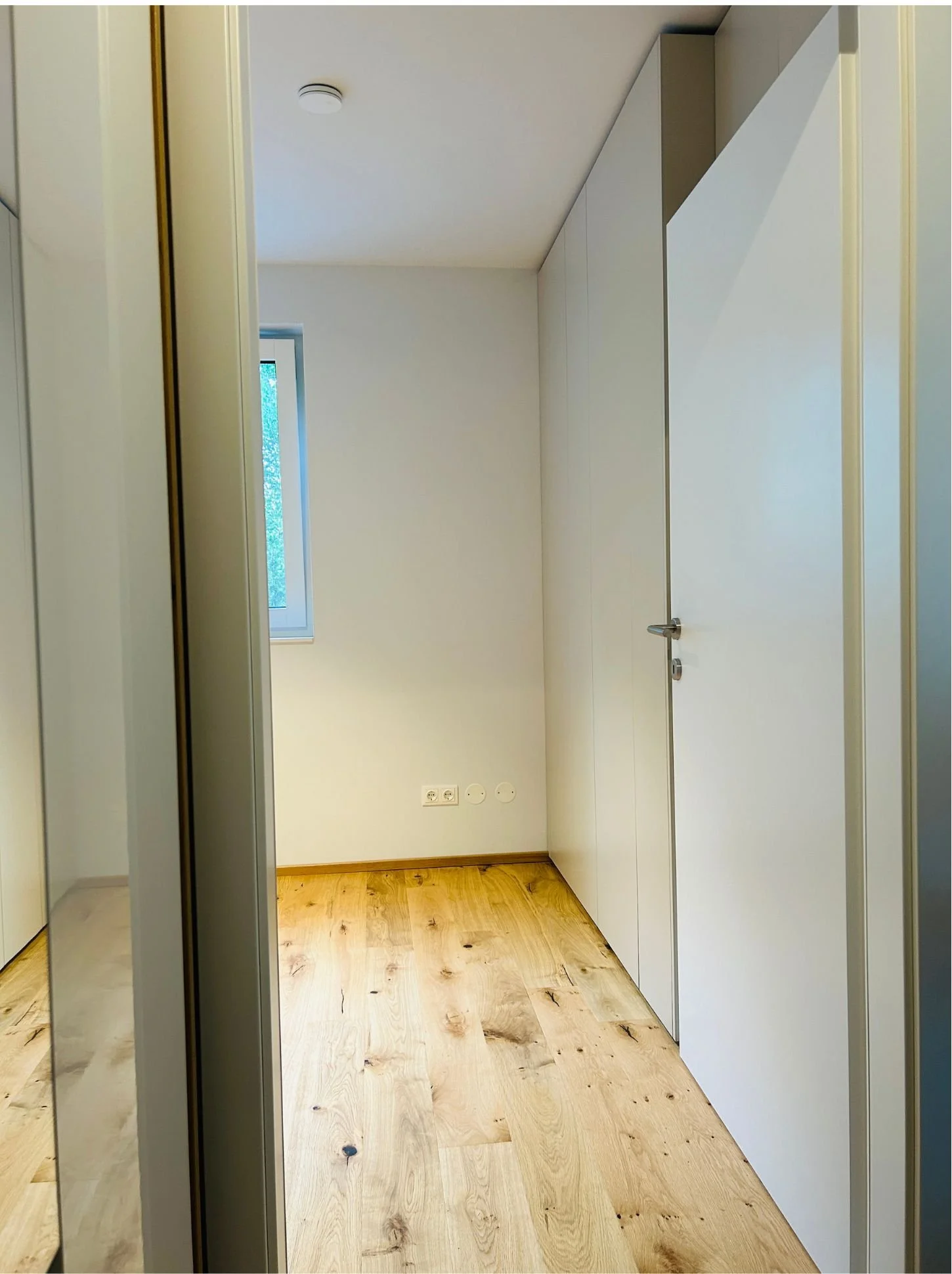 Schmaler, noch leerer Raum mit Holzboden und Fenster vor dem Einbau eines Schranks.