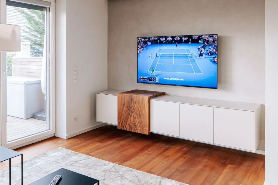 Helles Wohnzimmer mit TV in Wandnische, maßgefertigtem Lowboard aus Nussholz und weißen Schrankfronten, Parkettboden