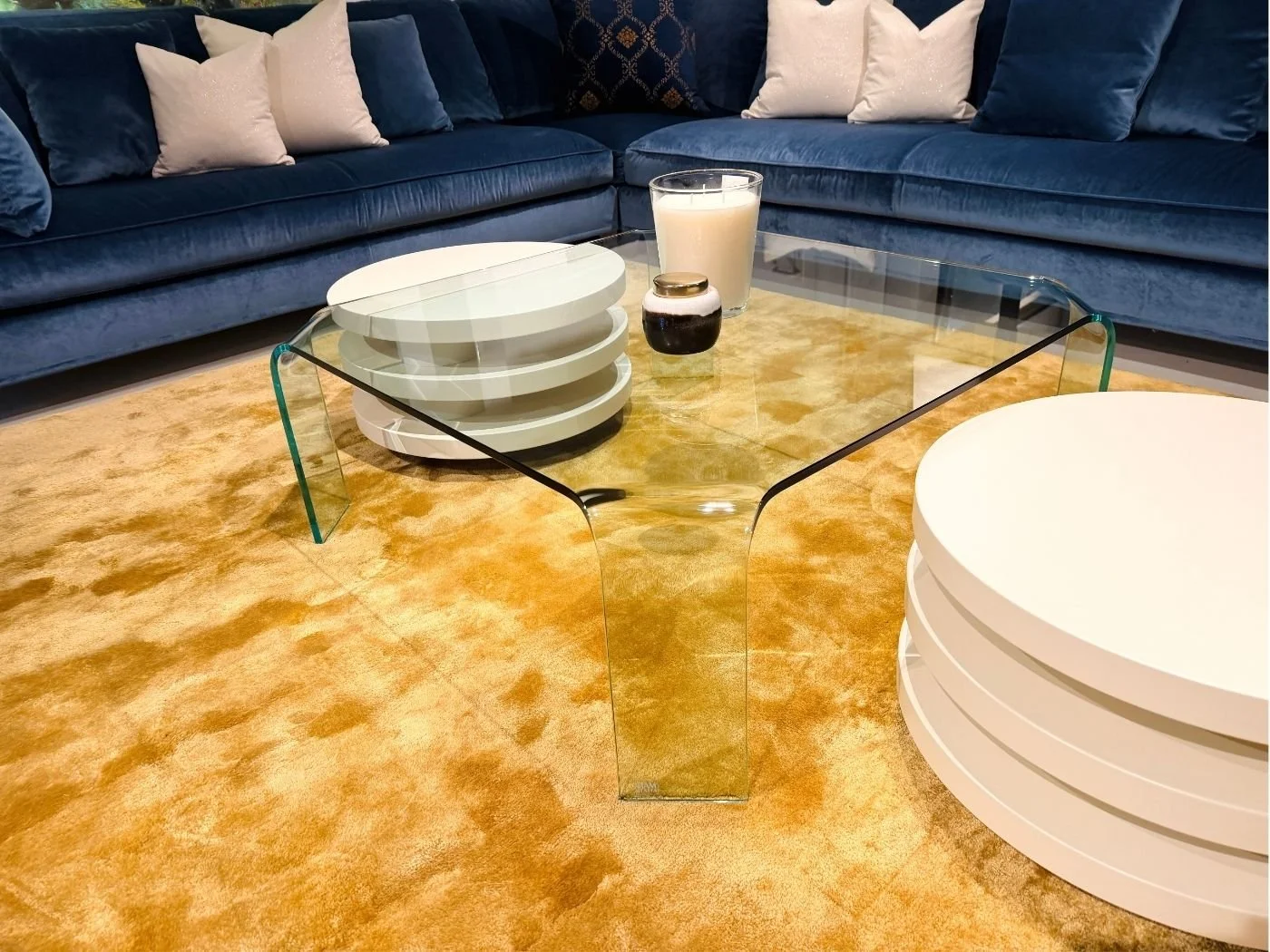 Wohnbereich mit dunkelblauem Ecksofa, gläsernem Couchtisch und ockerfarbenem Teppich