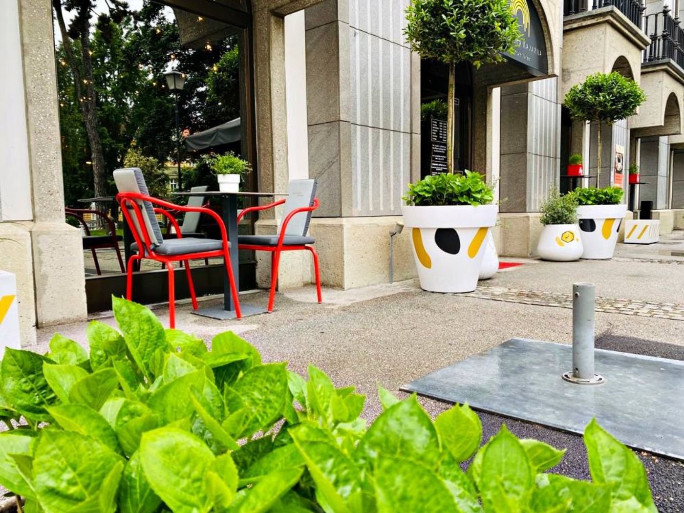 Stilvoller Restaurant-Außenbereich in der Gastronomie mit roten Stühlen, schwarzen Tischen und markanter Fassadenarchitektur - einladende Terrasse mit urbanem Flair und grüner Vordergrundbepflanzung
