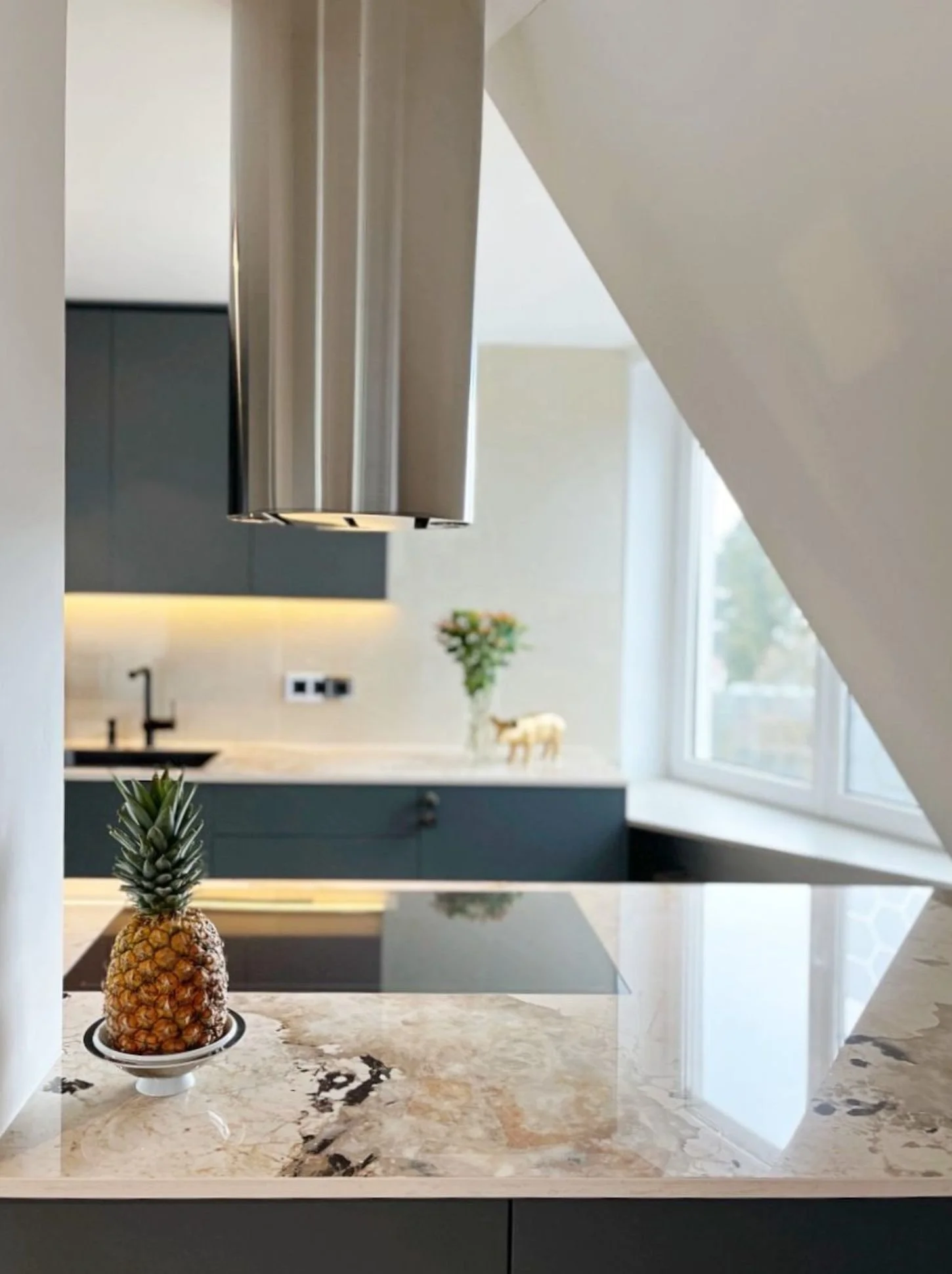Moderne Kücheninsel mit flächenbündigem Induktionskochfeld, heller Dekton-Arbeitsplatte von Cosentino als Modell Khalo und Edelstahl-Dunstabzug - hochwertige Küchenplanung und maßangefertigte Designküchen in Wien und Umgebung