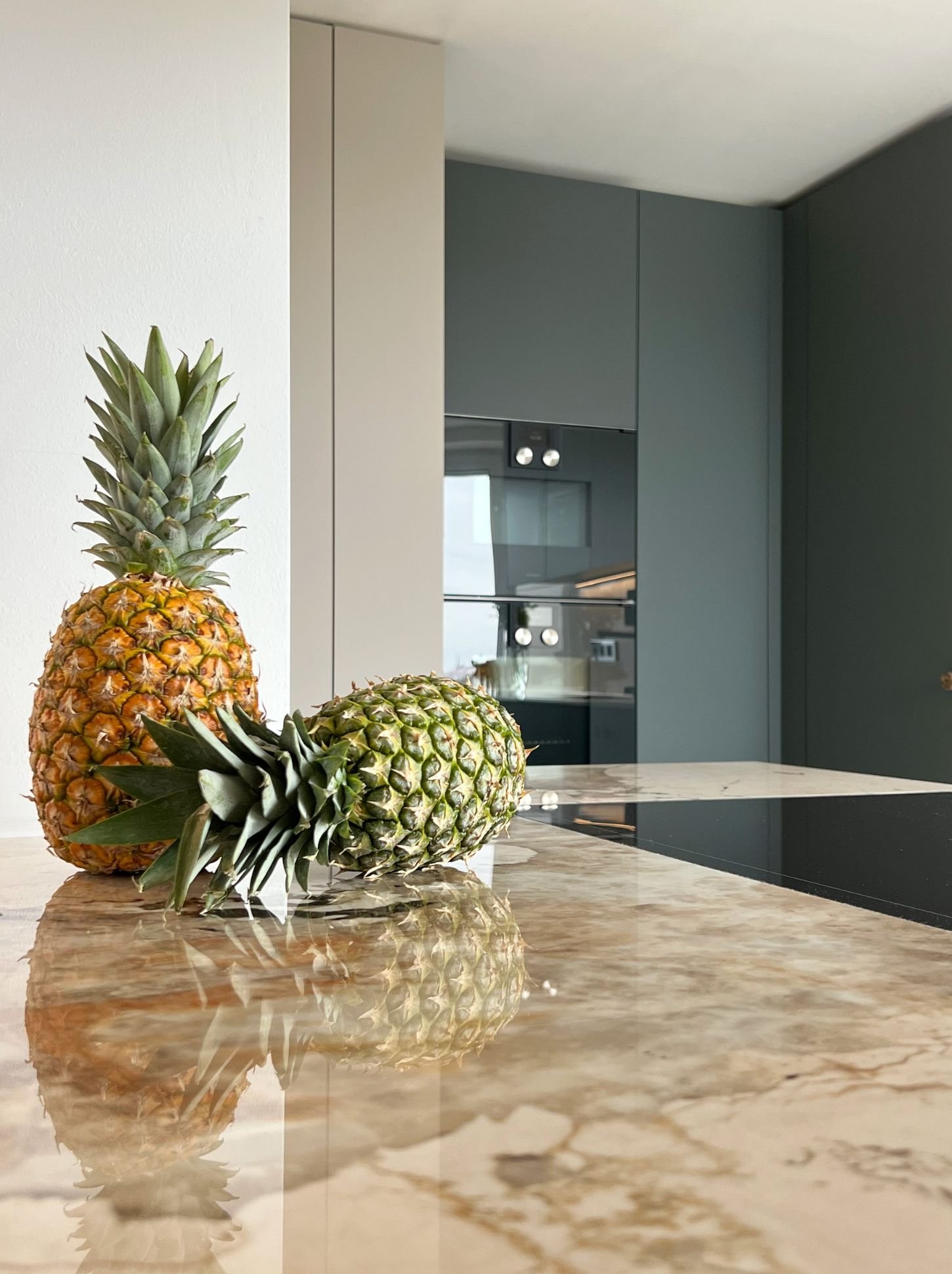 Moderne Küche mit dunklen Fronten, Steinplatte und Ananas auf der Arbeitsfläche.