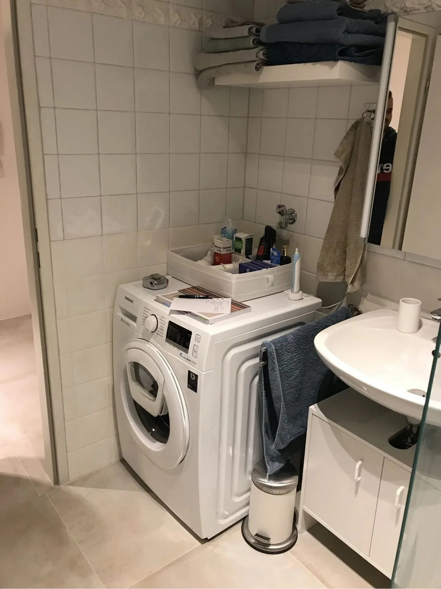 Vorher Foto eines kleinen, altmodischen Badezimmers mit Waschmaschine und Trockner neben dem Waschbecken, offene, unordentliche Ablage und Fliesen - Ausgangslage für Mini-Makeover