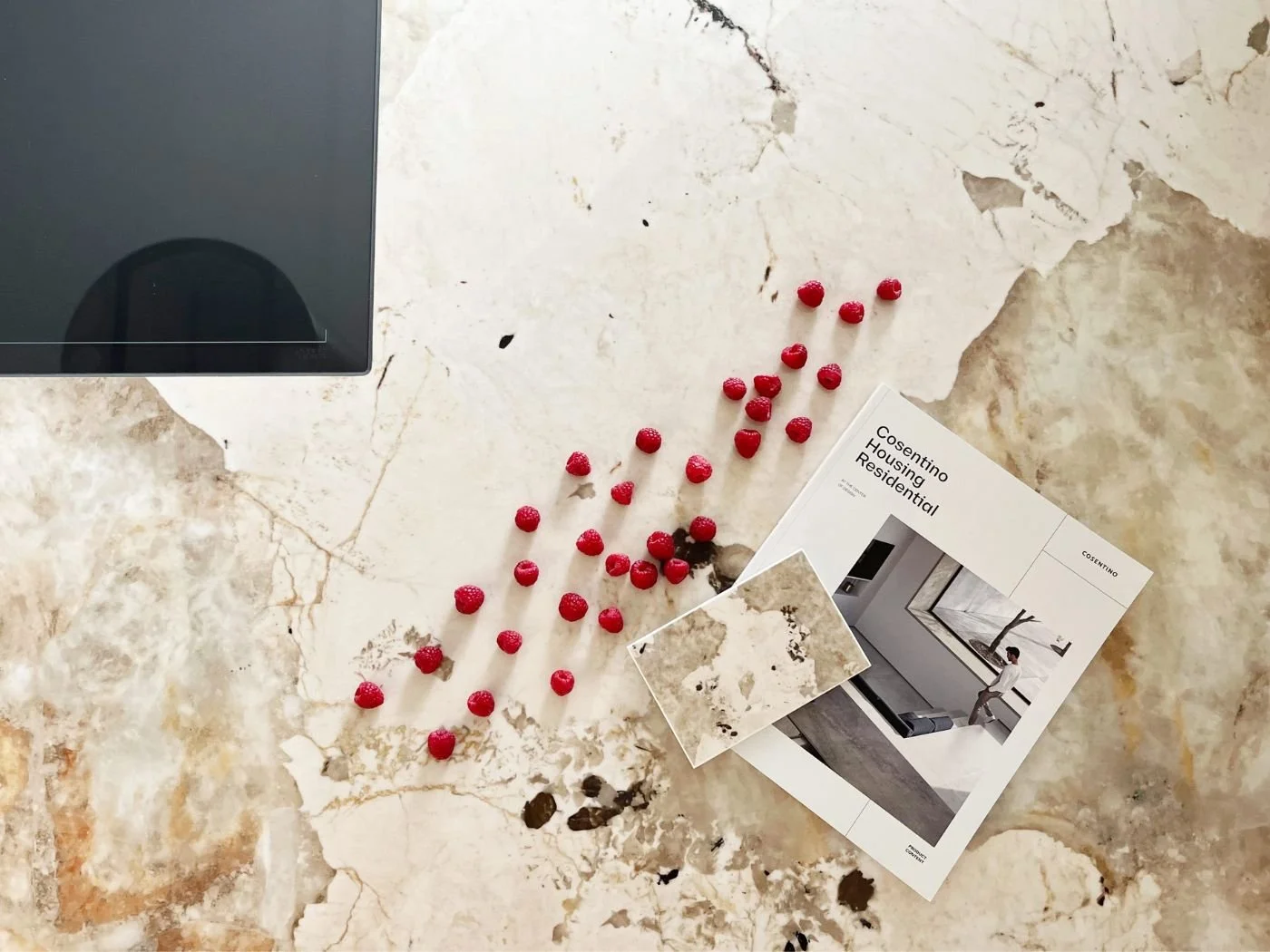 Detailaufnahme einer Dekton-Küchenarbeitsplatte der Serie Khalo von Cosentino mit flächenbündigem Induktionskochfeld, Himbeeren als Dekoration sowie Musterplatte und Planungsmappe - luxuriöses Küchendesign in Wien und Umgebung