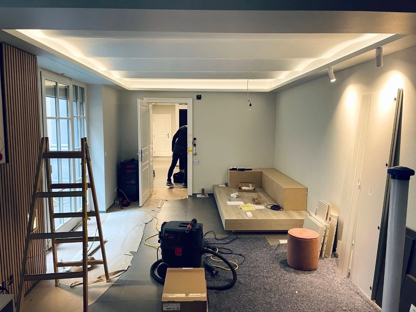 Wohnzimmer in der Umbauphase: moderne Luxus-Wohnraumgestaltung mit indirekter LED-Deckenbeleuchtung, maßangefertigter Sitzbank und Akustik-Holzpaneele
