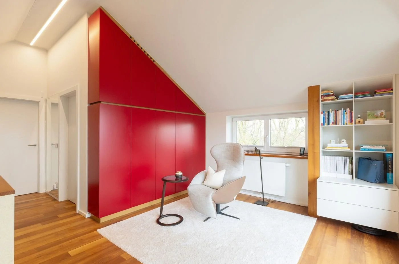 Roter Einbauschrank nach Maß unter der Dachschräge neben einem offenen Bücherregal