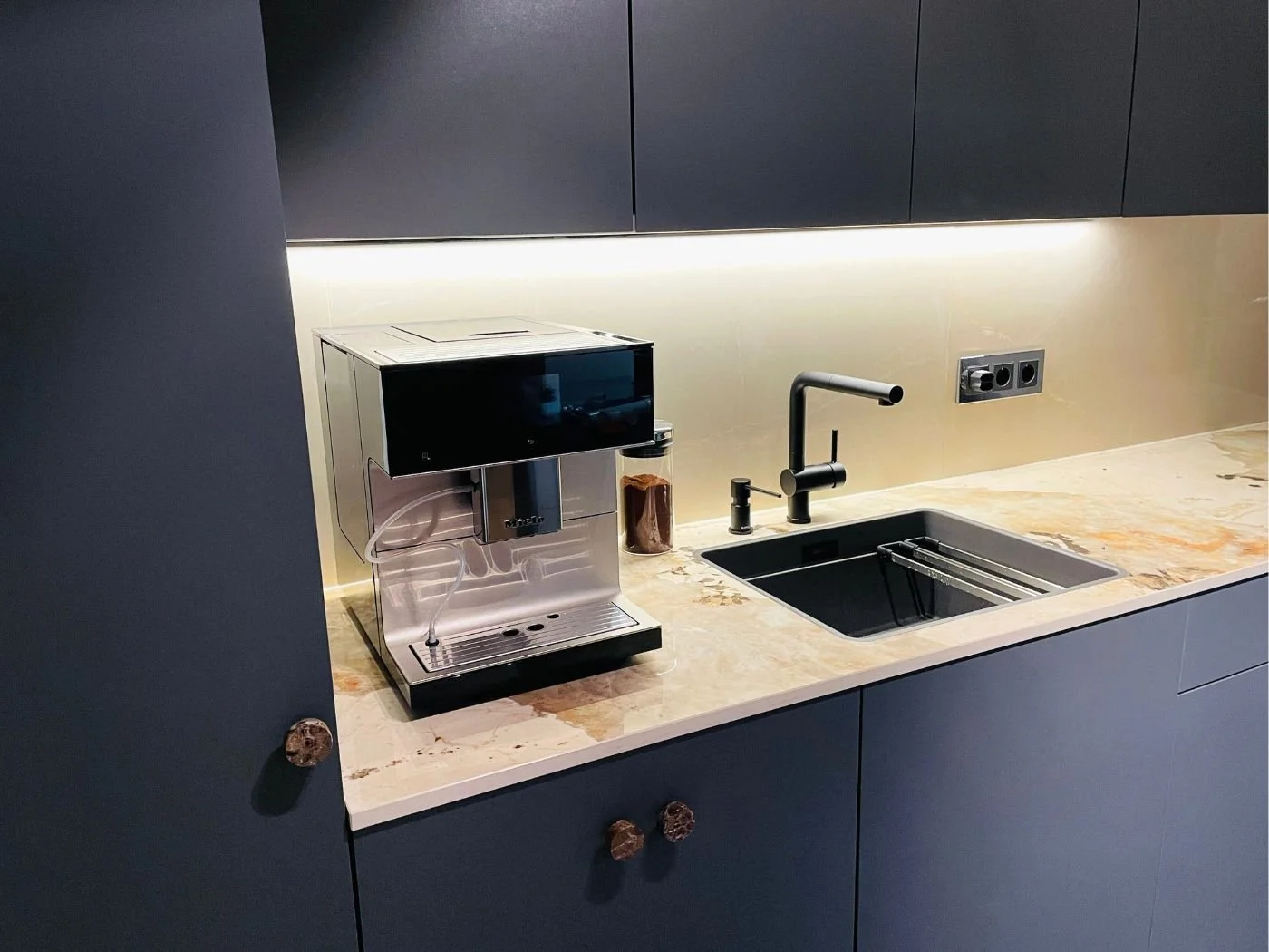 Spülenbereich in einer modernen Einbauküche mit flächenbündiger Spüle, dunkler Armatur und edlem Kaffeevollautomaten auf heller Dekton-Küchenarbeitsplatte Khalo der Firma Cosentino - maßangefertiges Küchendesign in Wien und Umgebung