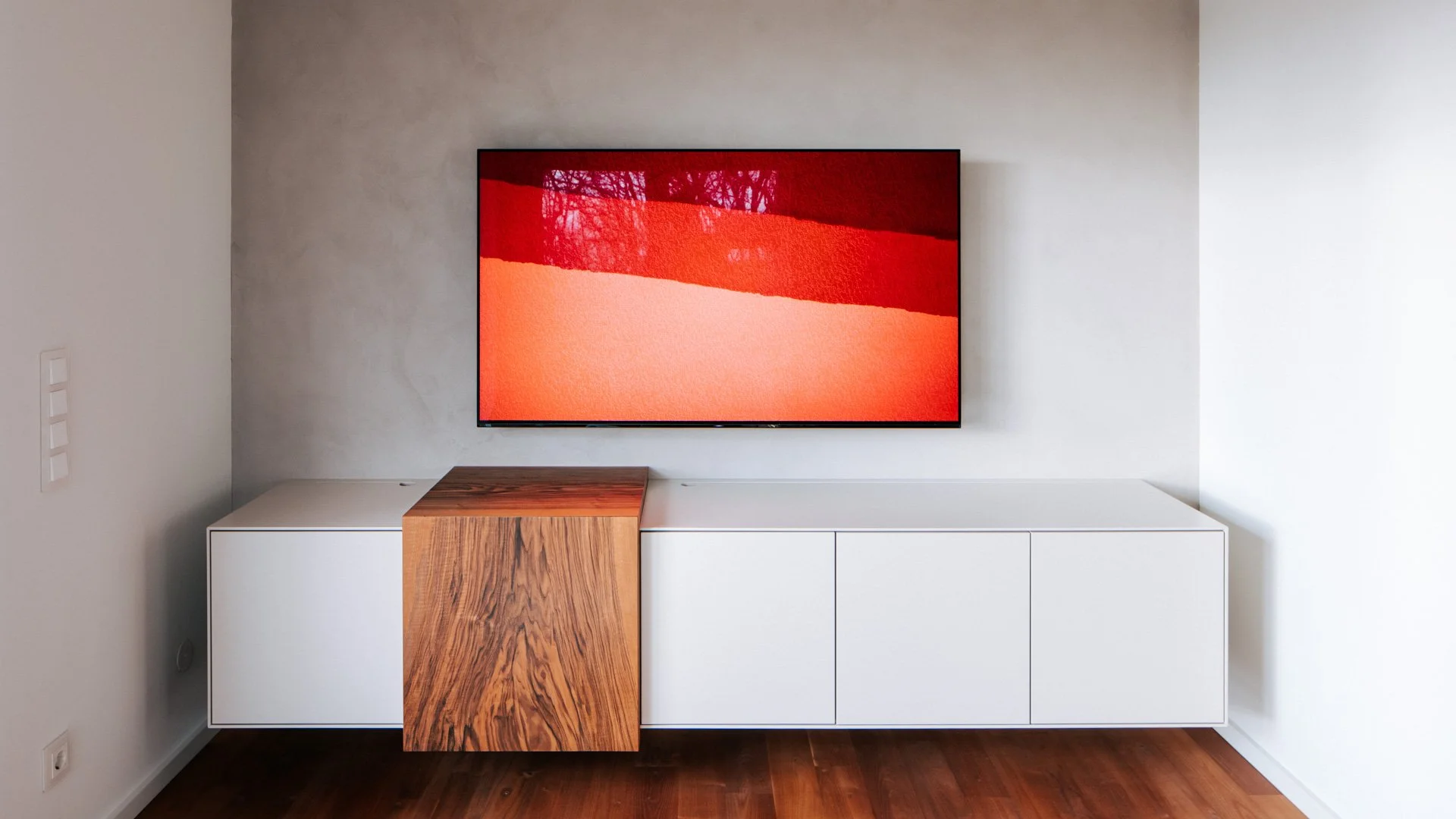 Wohnzimmer mit Fernseher über einem weißen Lowboard und einem Element aus gemasertem Holz.