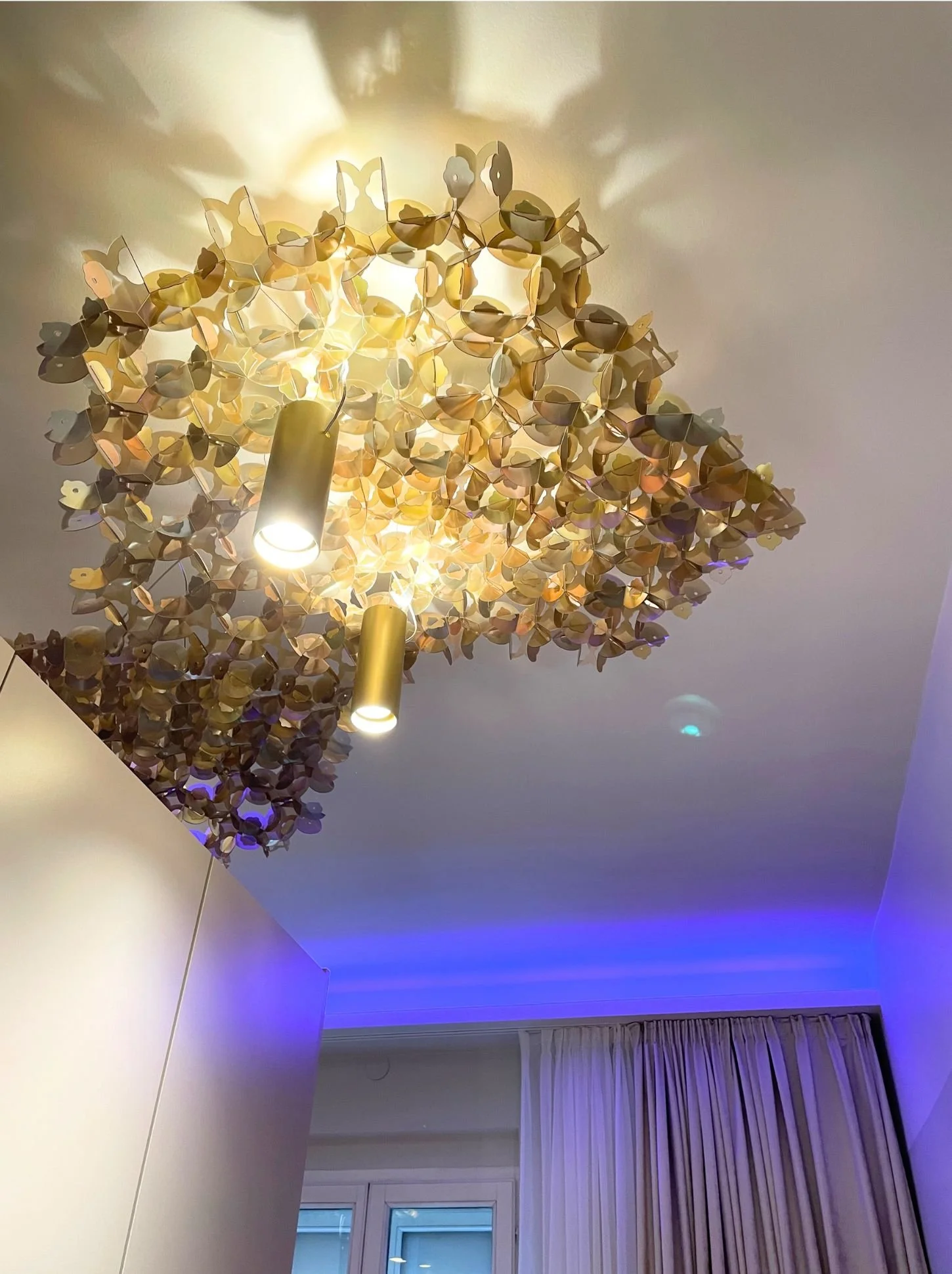 Goldene Designer-Deckenleuchte im Schlafzimmer mit indirekter LED-Stimmungsbeleuchtung (blau) und Vorhängen - modernes Luxus-Interior, Renovierung und Innenraumgestaltung von Paddy Artist Design GmbH