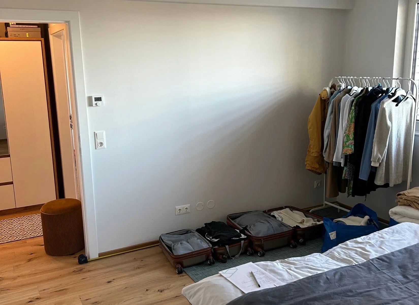 Schlafzimmer mit Ankleidebereich, Kleiderstange, Holzboden und schlichter Wandgestaltung, welches unordentlich ist
