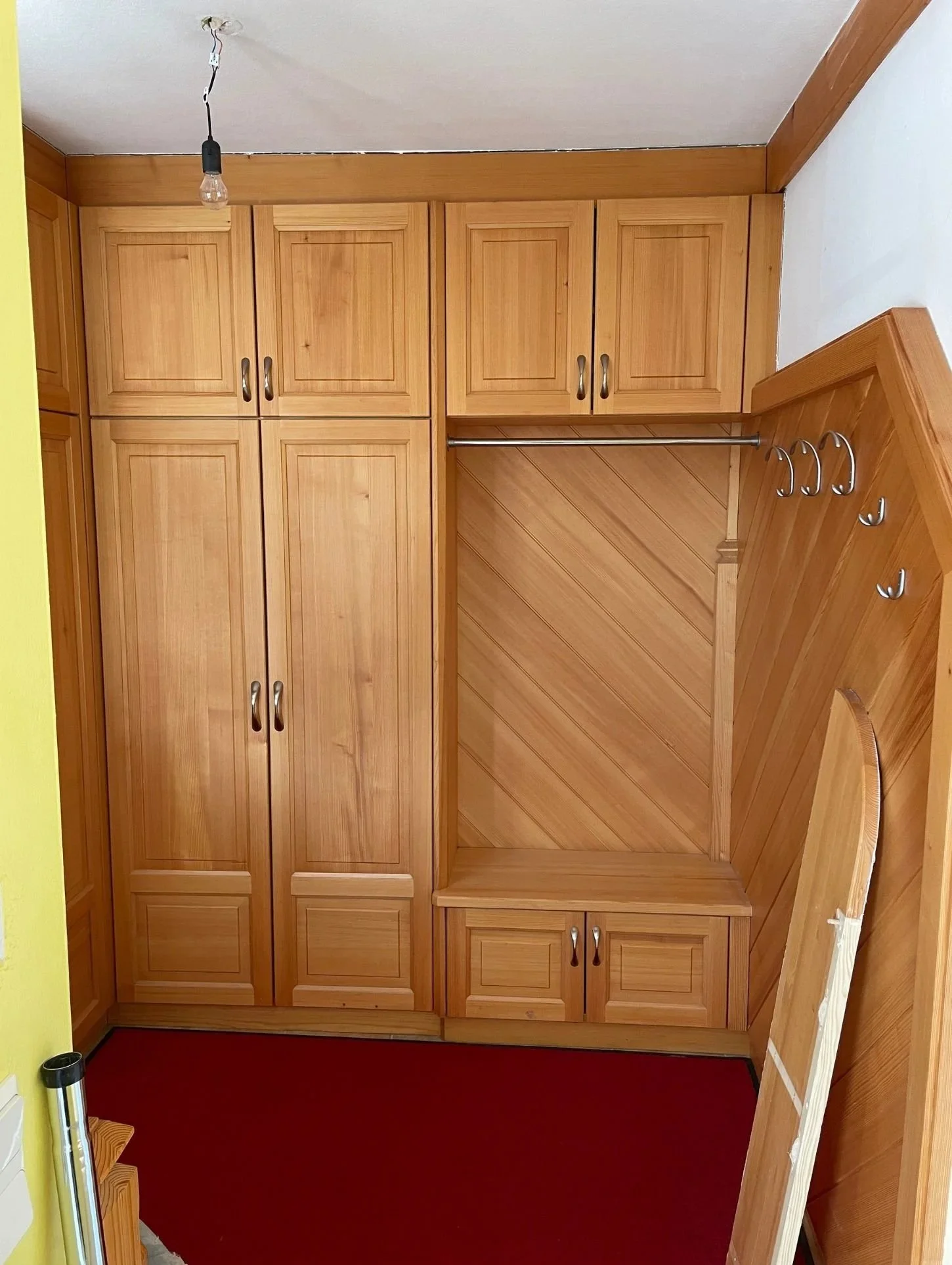 Ein alter Kleiderschrank aus Holz in einem Raum mit roten Teppichboden und weißen Wänden.