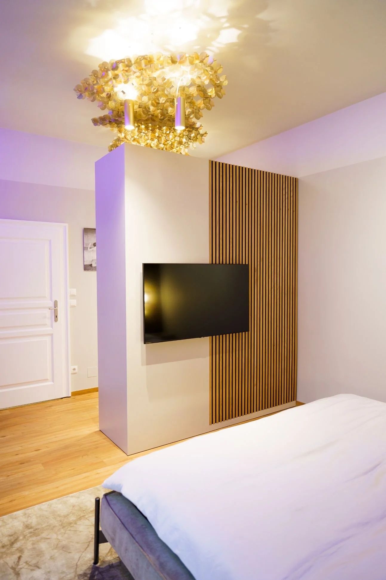 TV-Wand mit vertikalen Holzlamellen als Raumteiler im Schlafzimmer
