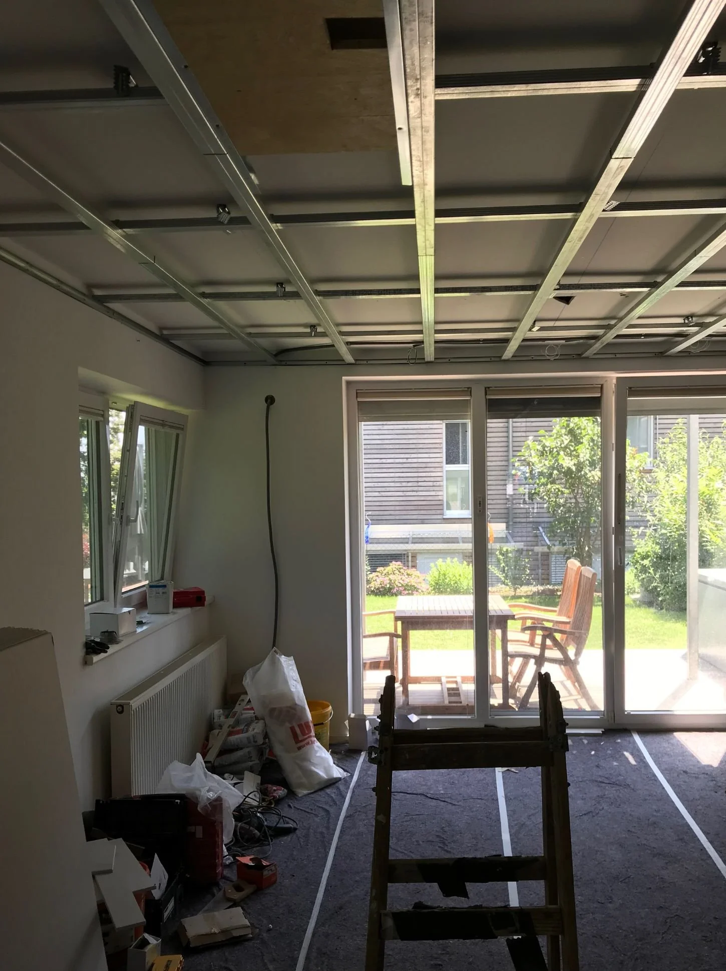 Wohnzimmer im Umbau mit Deckenunterkonstruktion, Innenausbau, offener Raumstruktur und Blick in den Garten während der Bauphase
