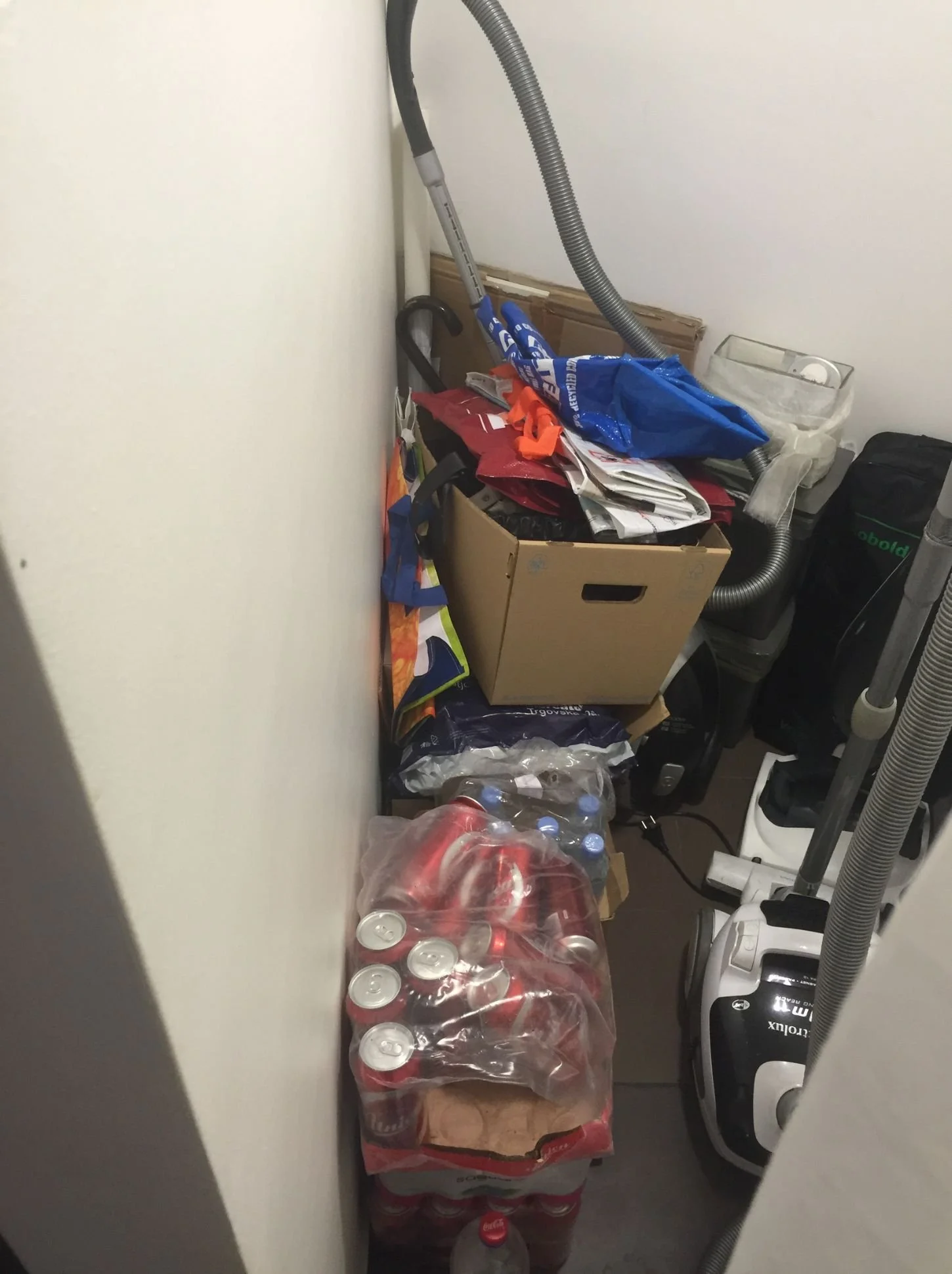 Vorher-Foto einer schmalen Nische als Stauraumproblem: unordentliche Abstellfläche mit Kartons, Getränkekisten und Staubsauger - Ausgangssituation für Stauraumplanung und maßgefertigte Schranklösung