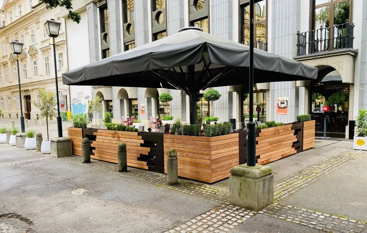 Gastgarten mit großem schwarzem Sonnenschirm und Pflanztrögen aus Holz als Abgrenzung
