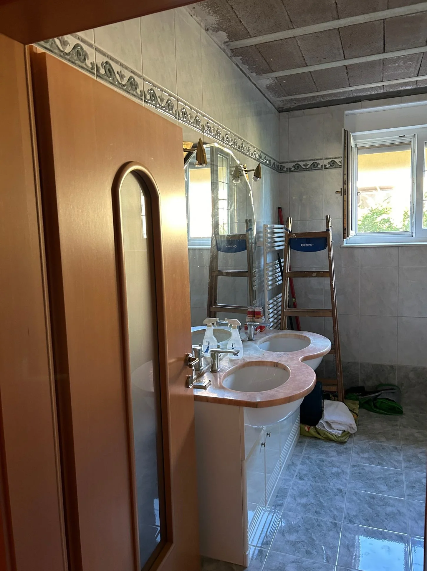Vorher-Foto eines altmodischen Badezimmers mit blau-grauen Fliesen, Doppelwaschbecken und älterer Ausstattung - Ausgangssituation für Badrenovierung und Modernisierung