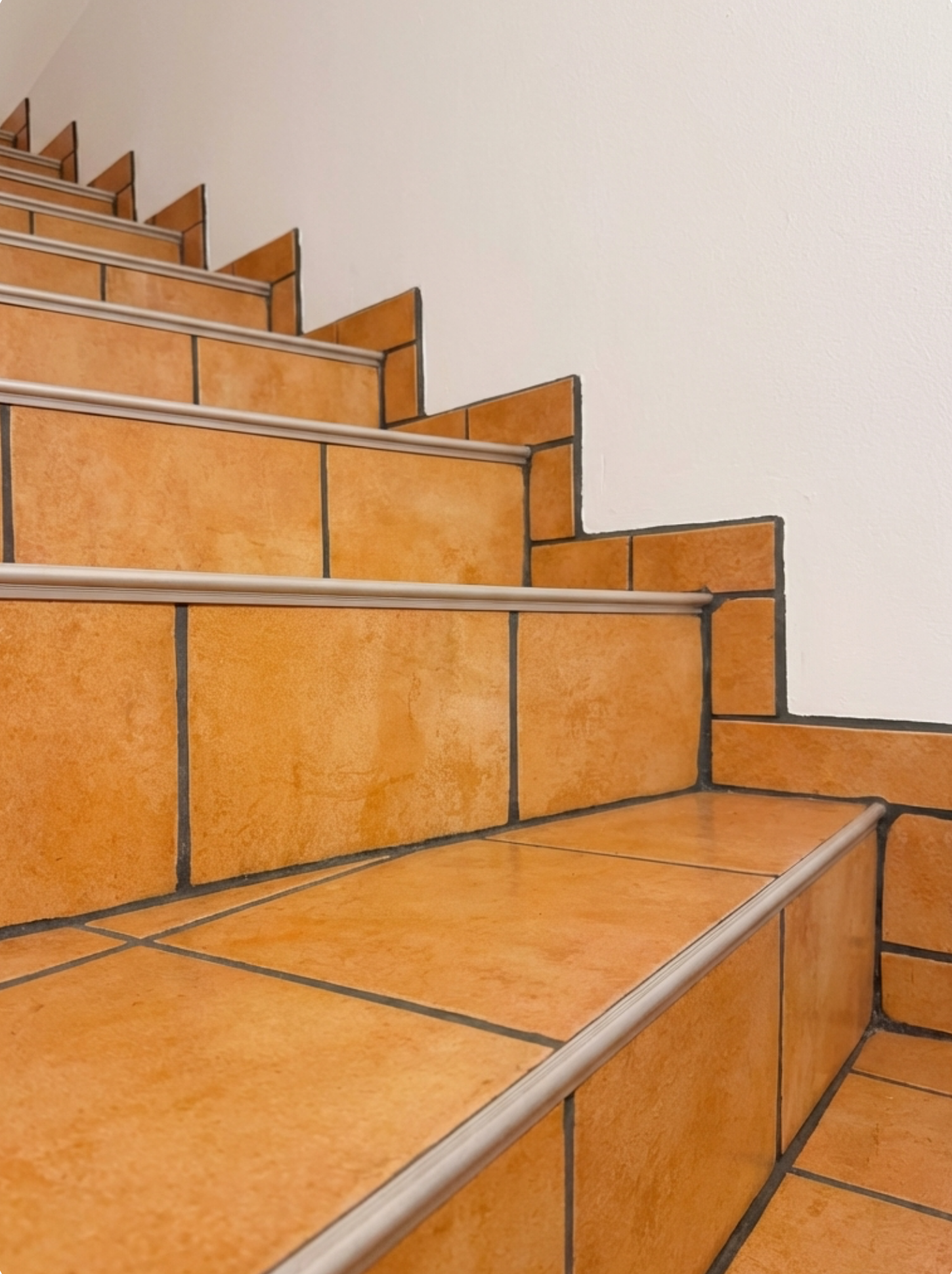Vorher-Bild eines Kellergangs mit Treppe und orangen Fliesen als Ausgangssituation vor einer fugenlosen Umgestaltung