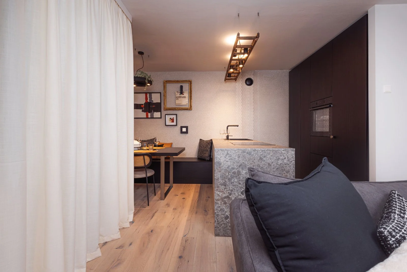 Offener Wohnbereich mit grauem Sofa, Holzboden und kompakter Küche mit dunklen Einbauschränken