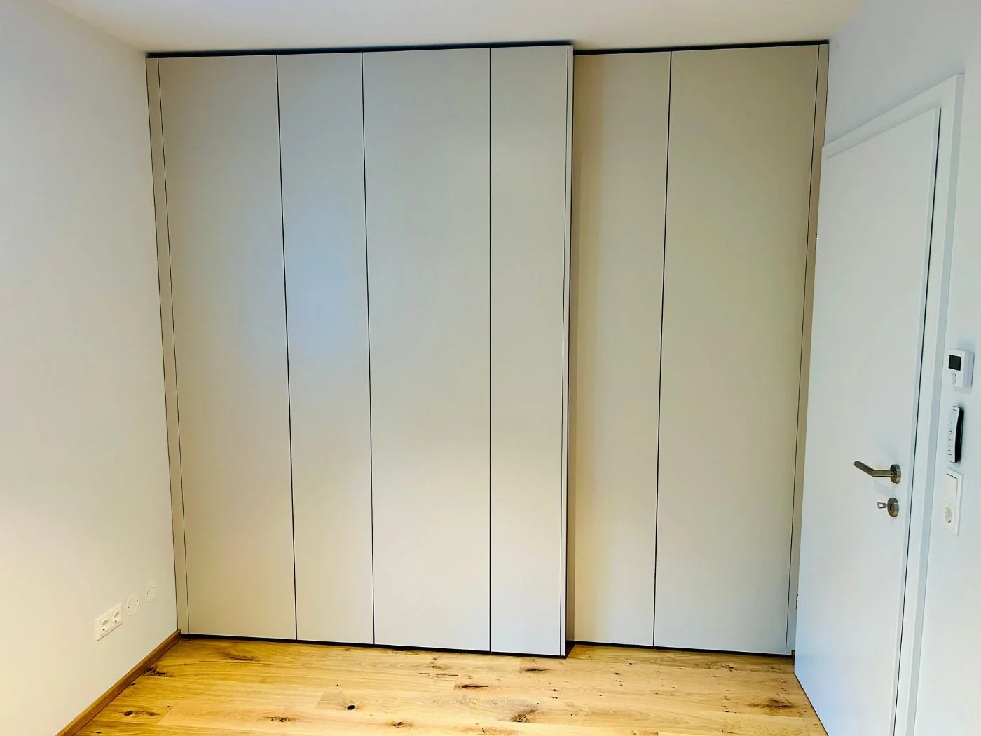 Raumhoher weißer Einbauschrank mit mehreren Türen in einem schmalen Raum.