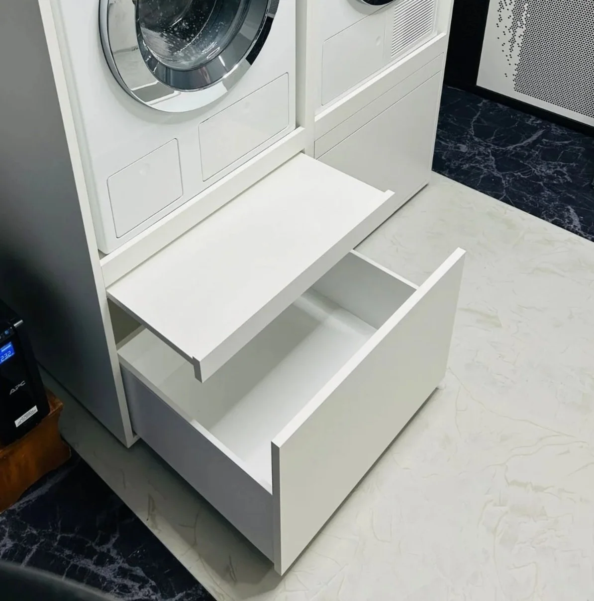 Offene weiße Schublade unter einer Waschmaschine in einer modernen Waschküche.