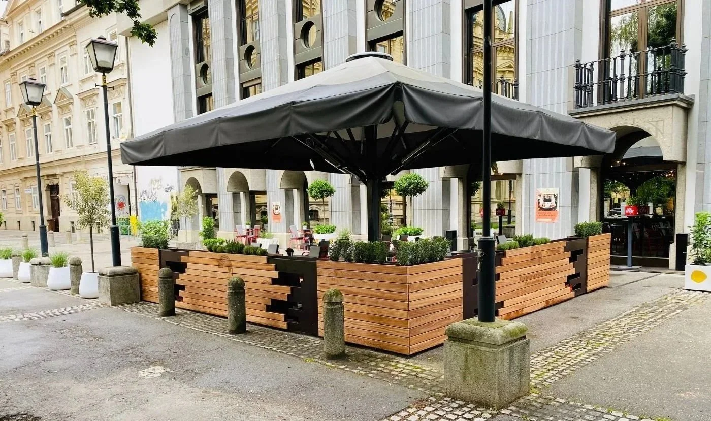 Gastgarten mit großem schwarzem Sonnenschirm und Pflanztrögen aus Holz als Abgrenzung